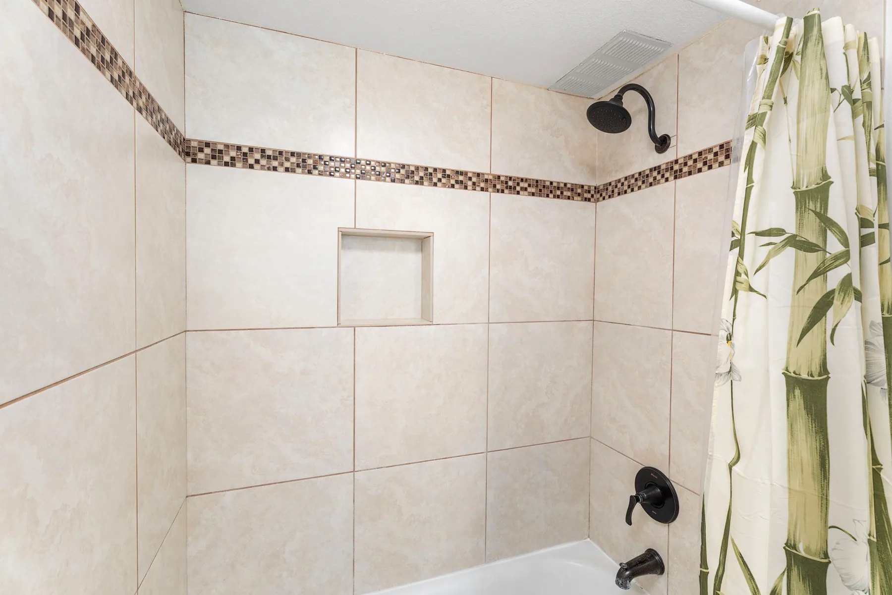 Una ducha de baño alicatada con un nicho en la pared y una cortina estampada.