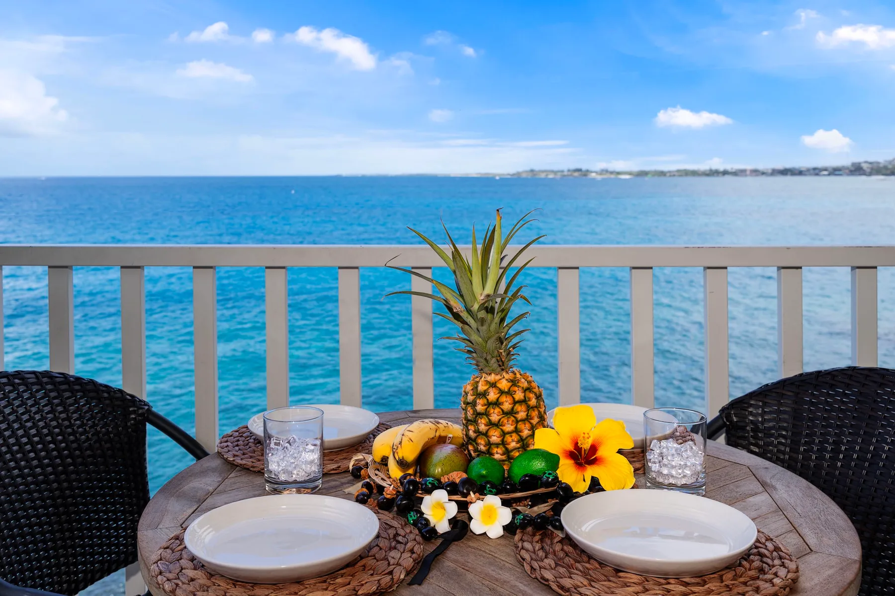 Una mesa junto al mar con fruta y flores da al océano.
