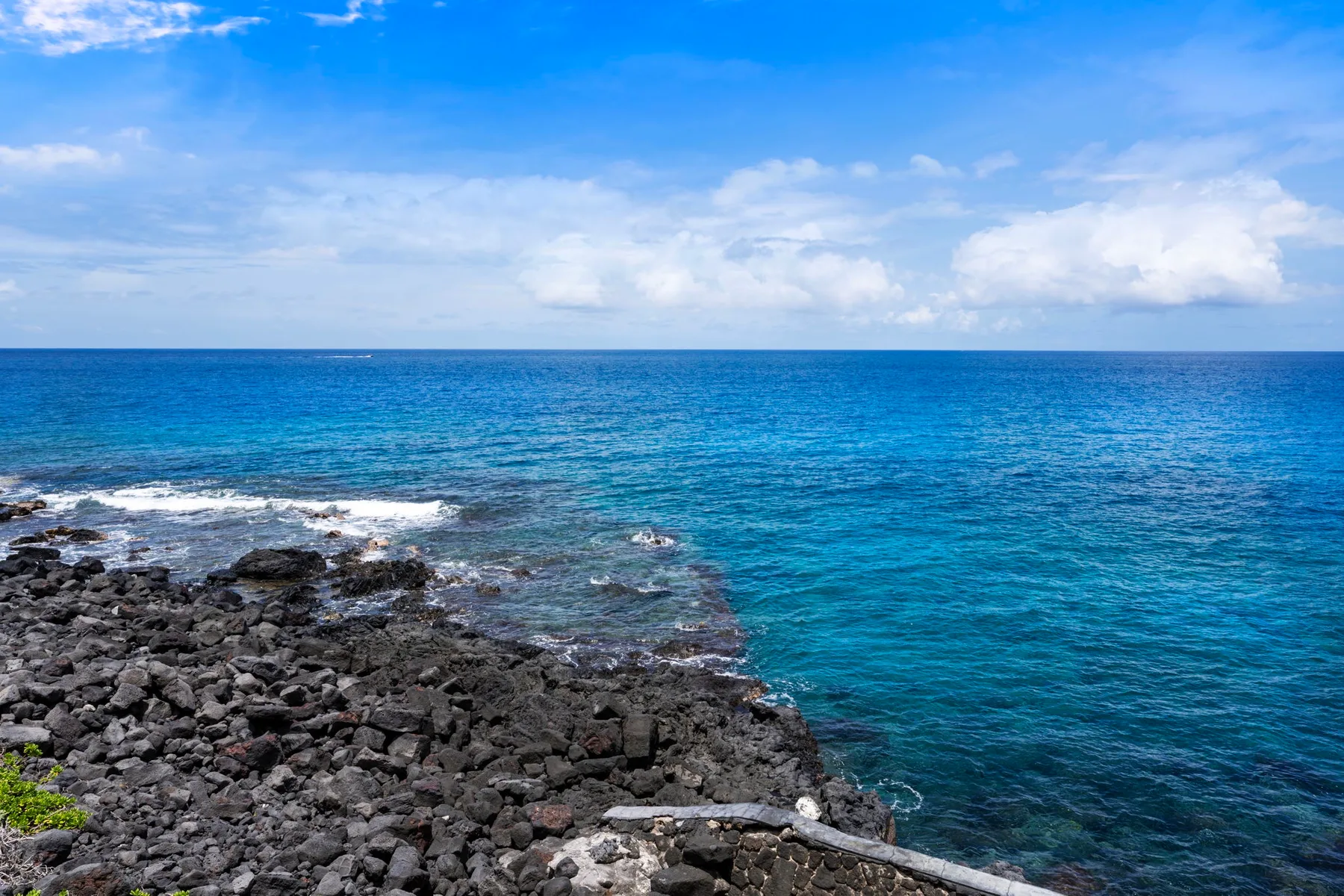 Una costa rocosa bordea el océano azul bajo un cielo parcialmente nublado.