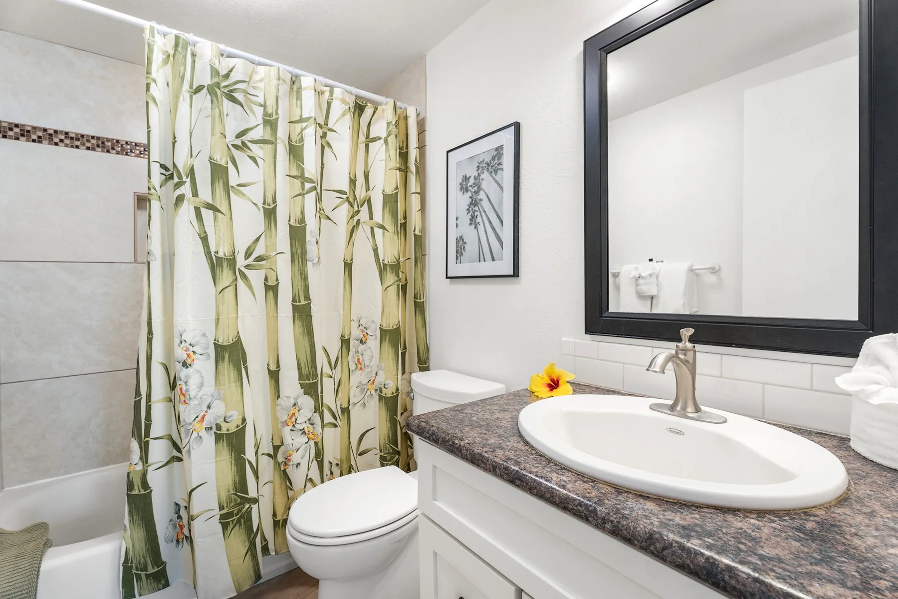 Un baño con lavabo, espejo, inodoro y cortina de ducha estampada.
