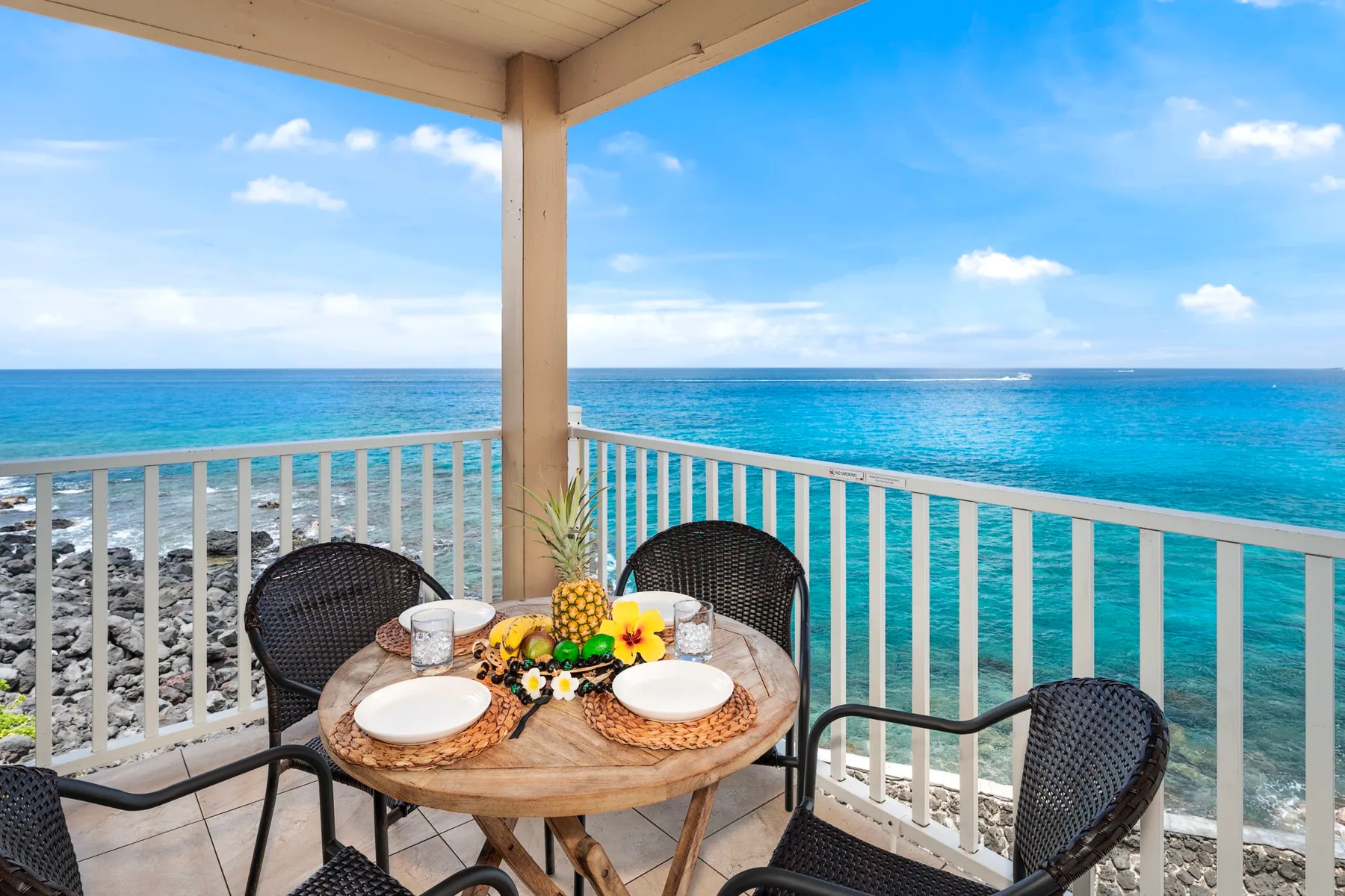 A covered seaside balcony with a round table and ocean view.