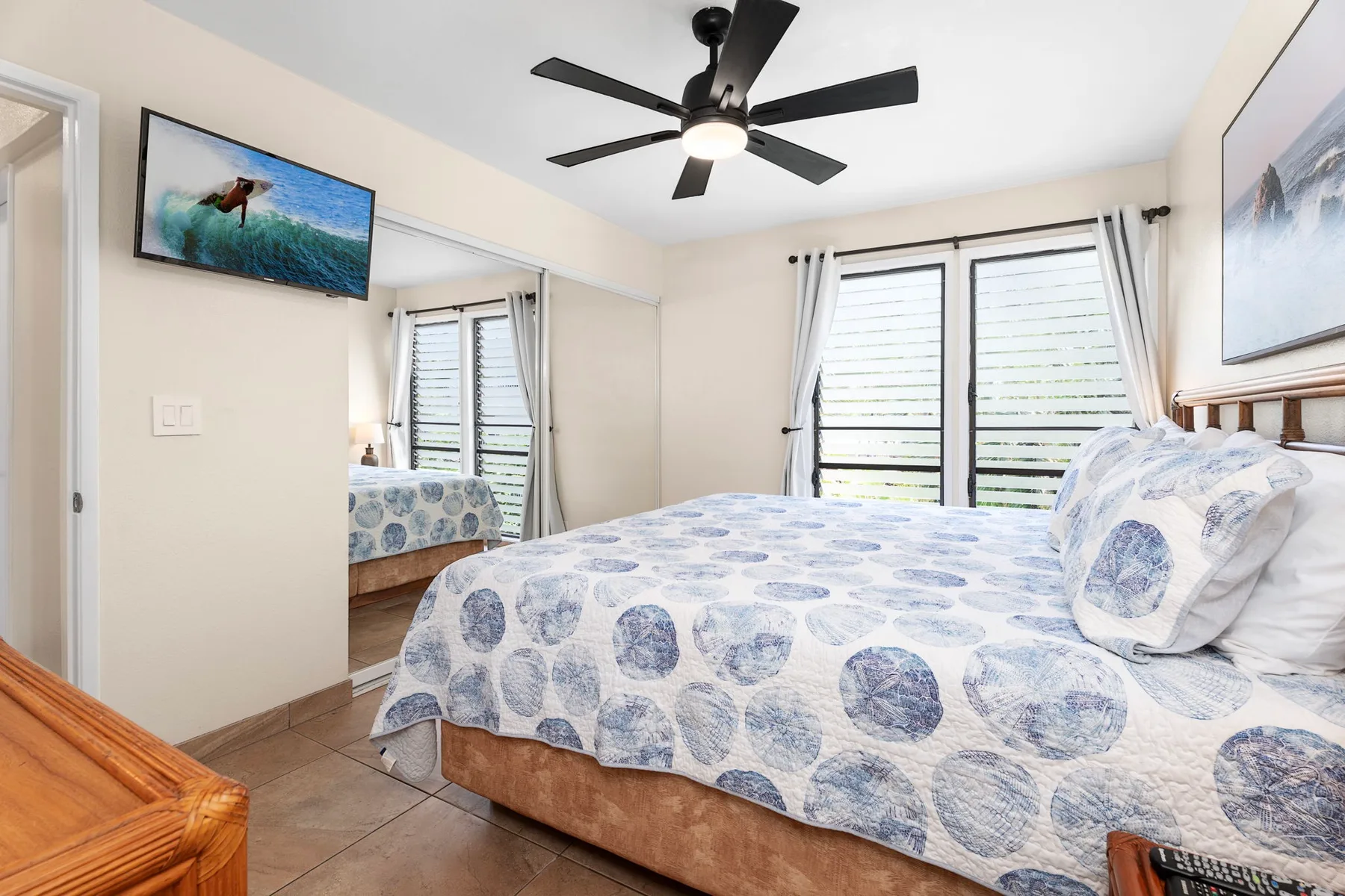 Un dormitorio con una cama cubierta con ropa de cama estampada azul y ventanas grandes.