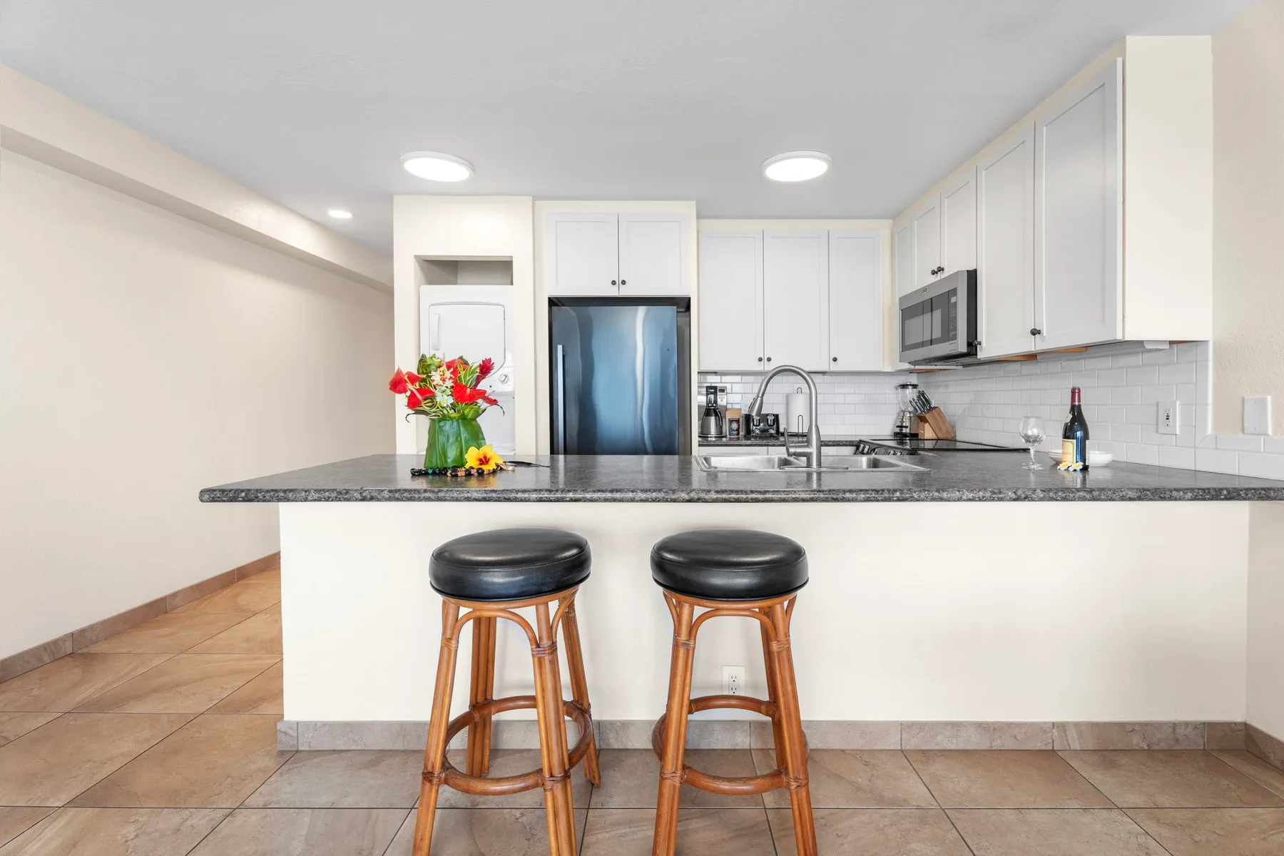 Una cocina luminosa con gabinetes blancos, una encimera oscura y dos taburetes.
