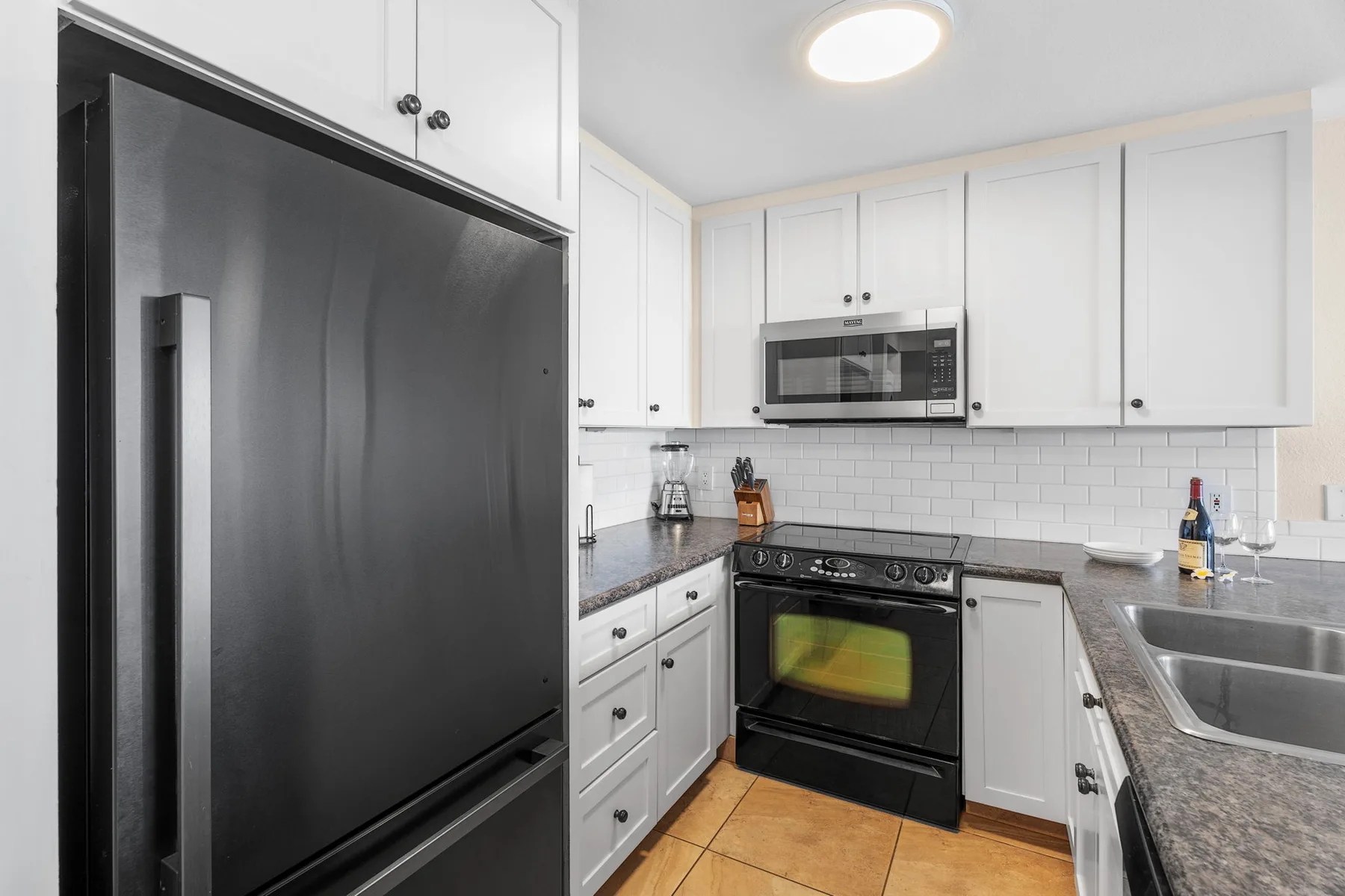 Una cocina luminosa con gabinetes blancos, un refrigerador negro y un horno.
