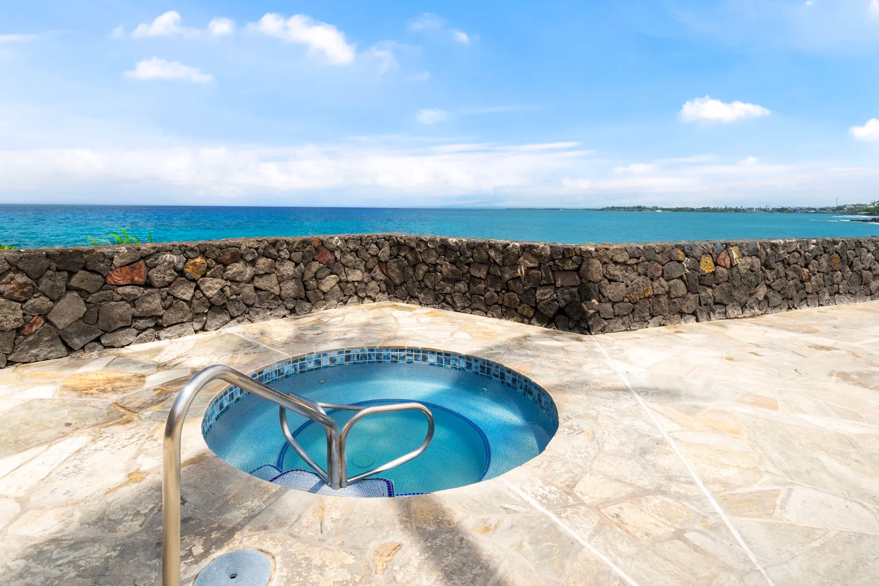 Una pequeña piscina circular está en una terraza de piedra con vistas al océano.