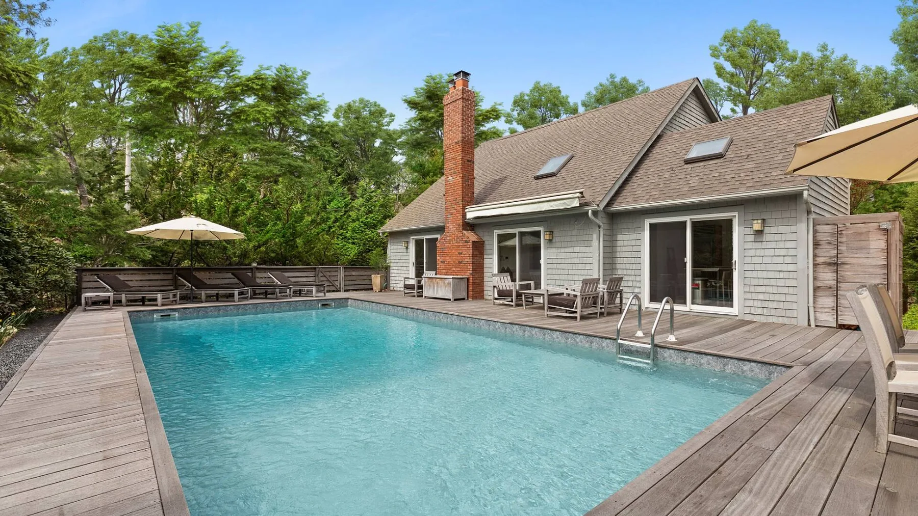 An outdoor swimming pool beside a house, surrounded by a wooden deck and trees.