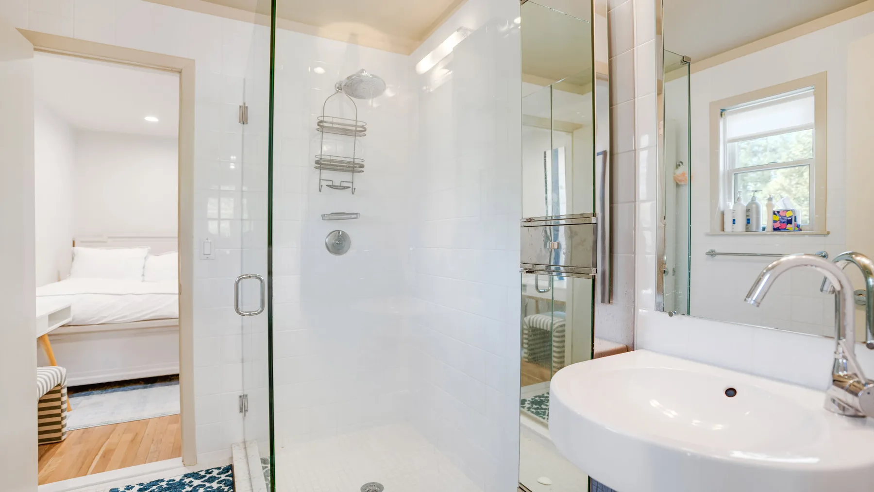 Un baño luminoso con una ducha de cristal y un lavabo blanco junto a una ventana.