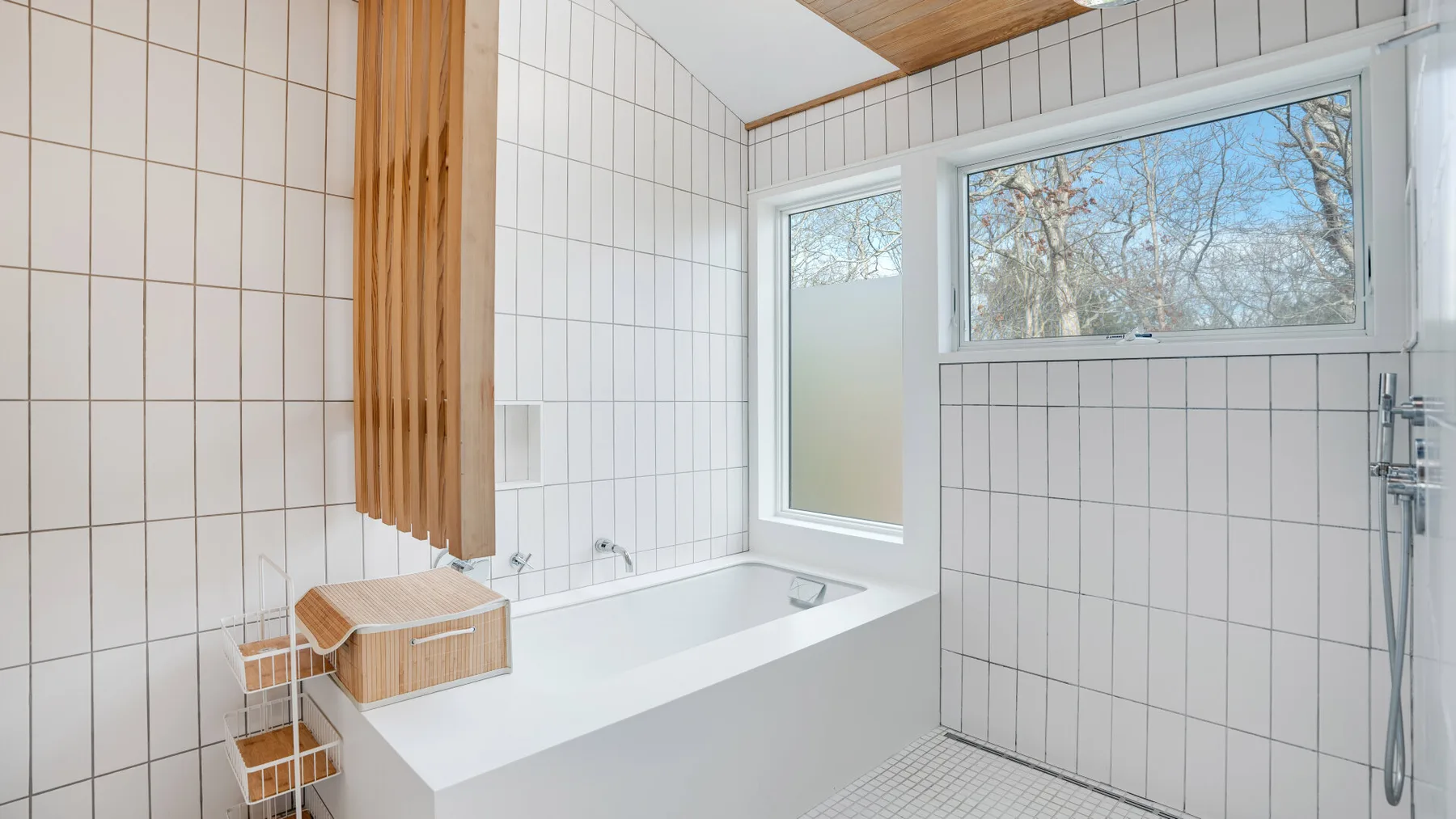 Un baño alicatado con bañera y una ventana grande con vistas a los árboles.
