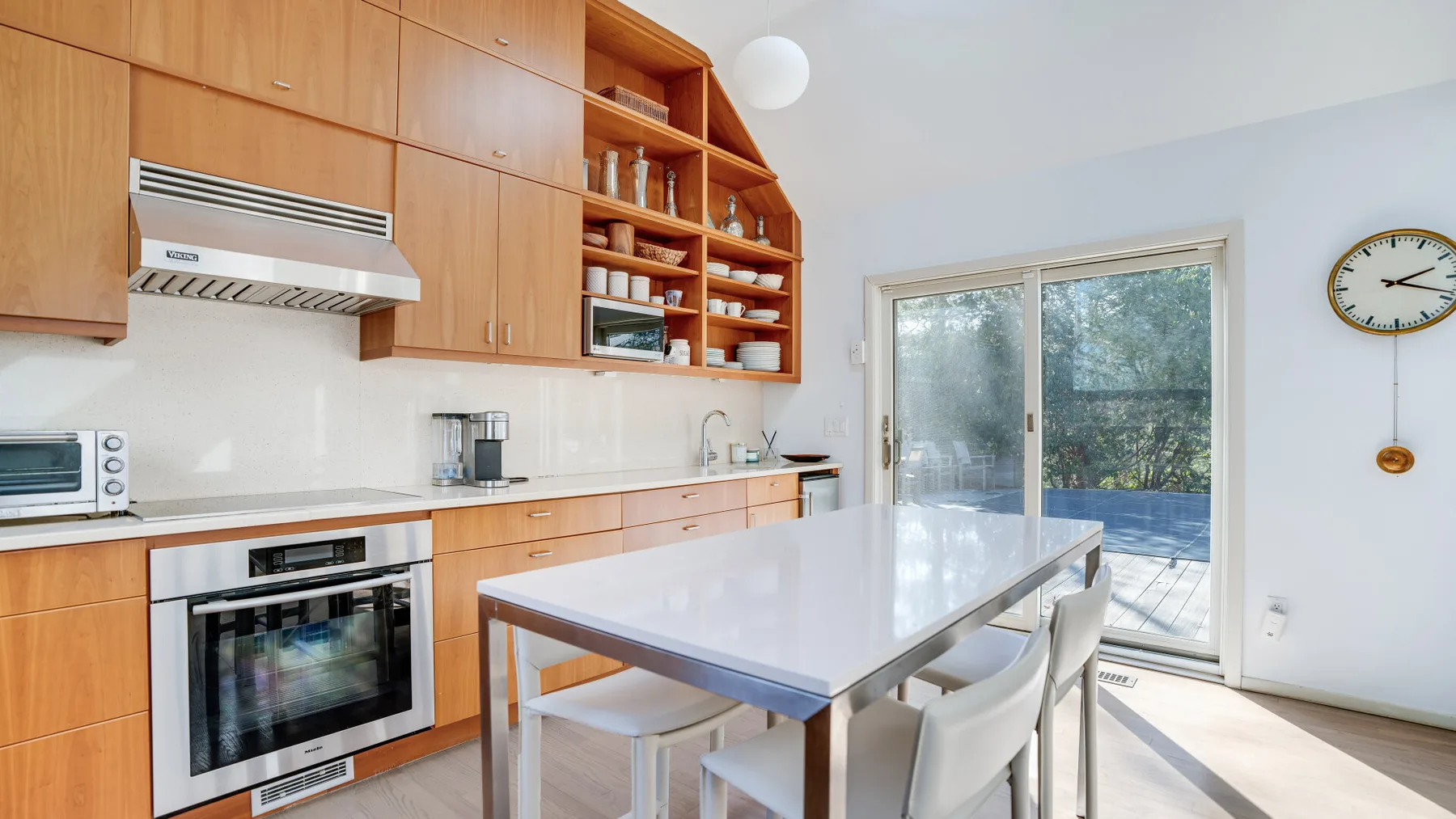 Una cocina luminosa con gabinetes de madera y una mesa larga junto a puertas de vidrio.