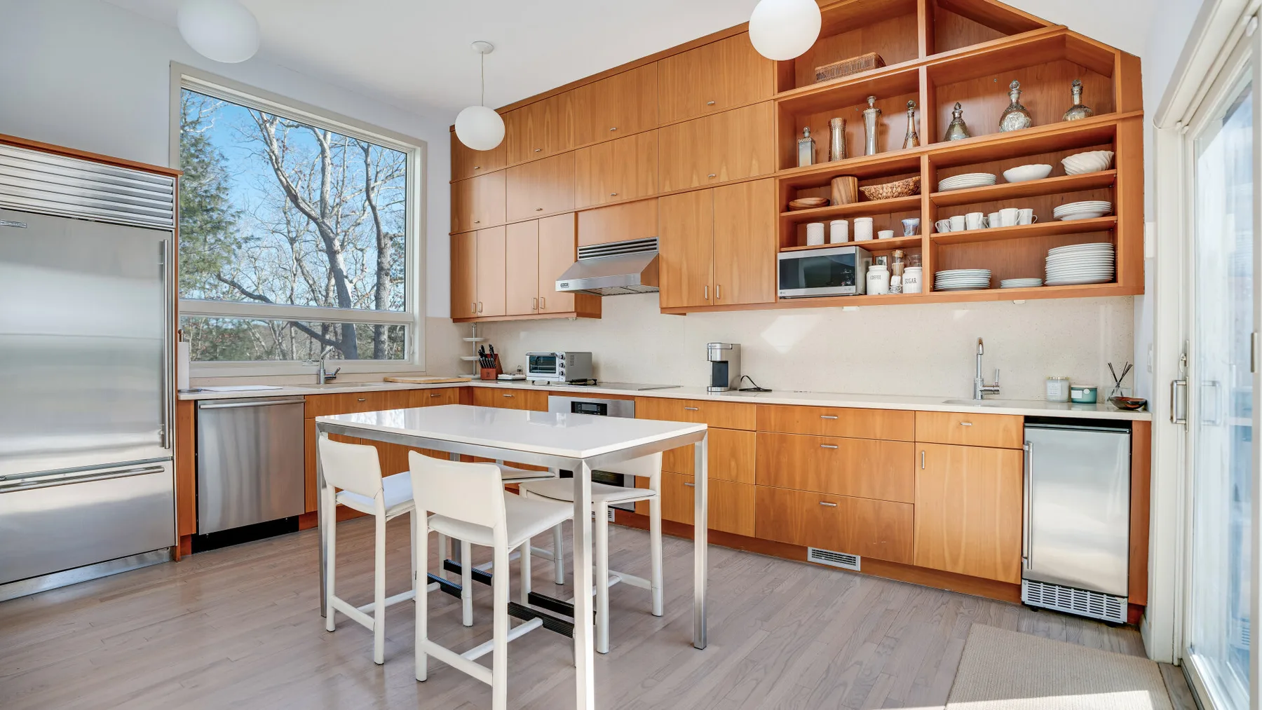 Una cocina luminosa con gabinetes de madera, una mesa central y grandes ventanas.