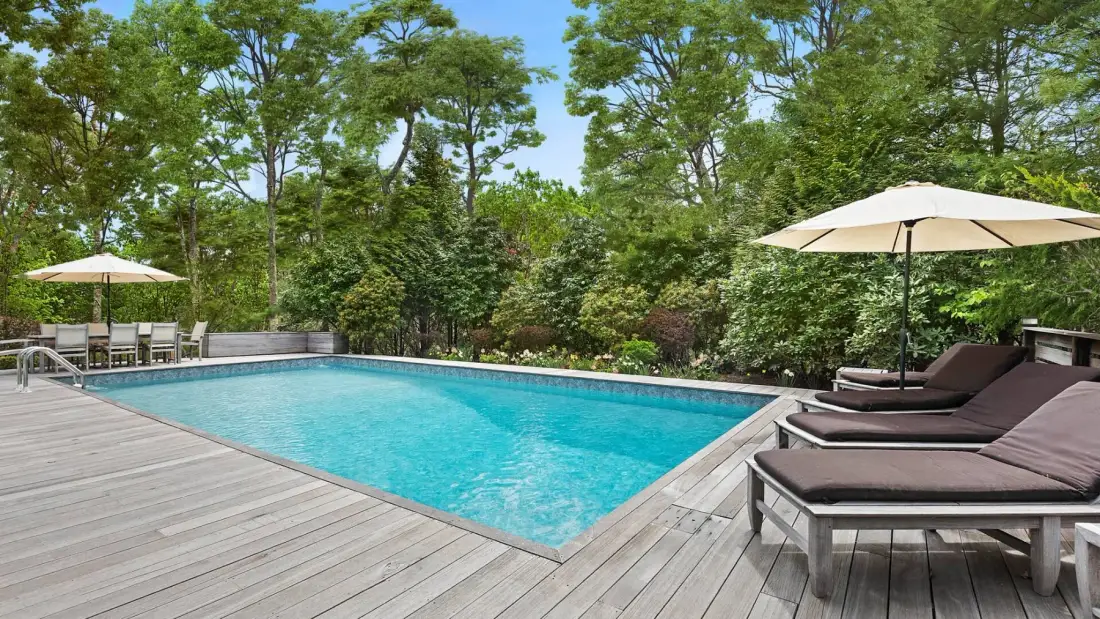 An outdoor swimming pool sits beside a wooden deck with loungers and trees.