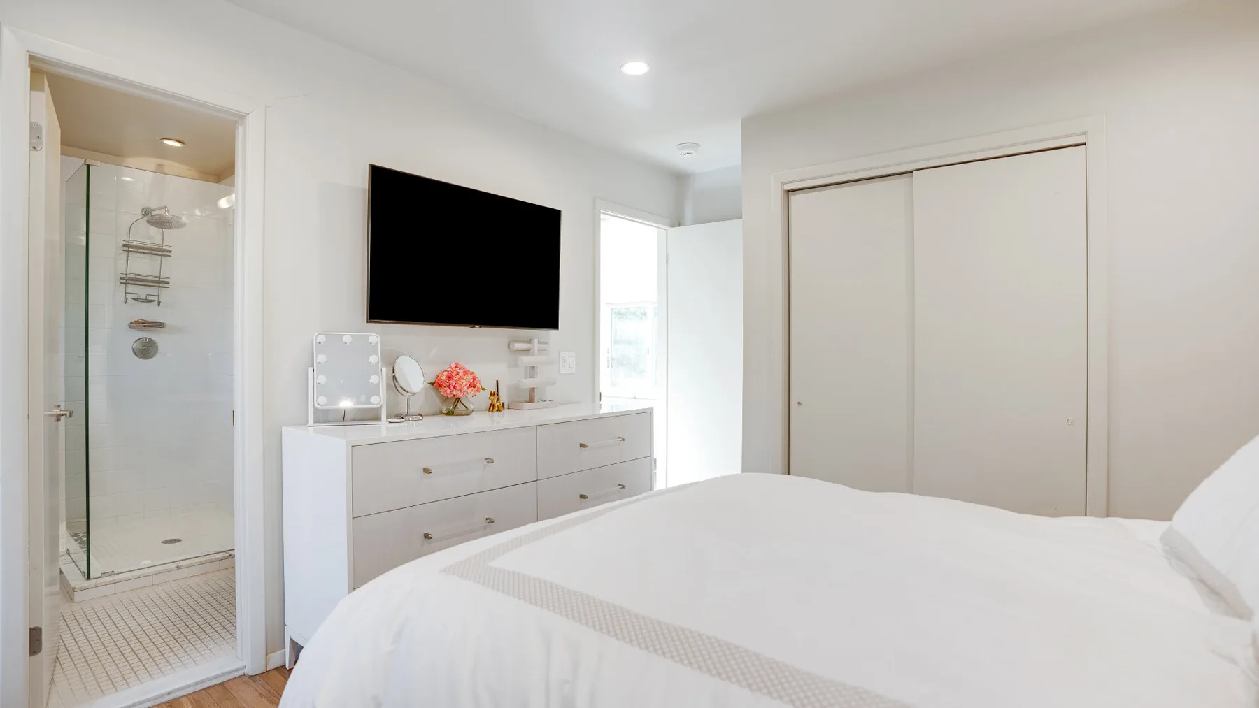 Un dormitorio luminoso con cama, cómoda y televisor montado en la pared.