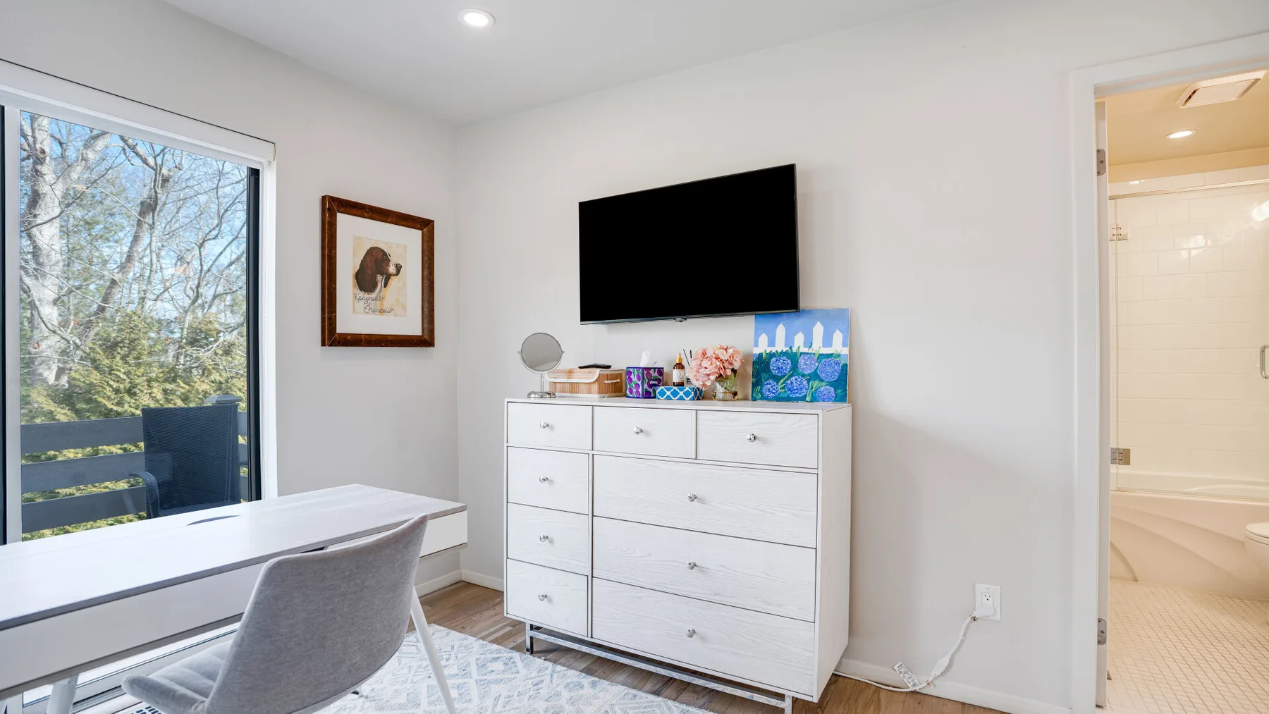 Un dormitorio con una cómoda, un televisor y un escritorio junto a una ventana grande.