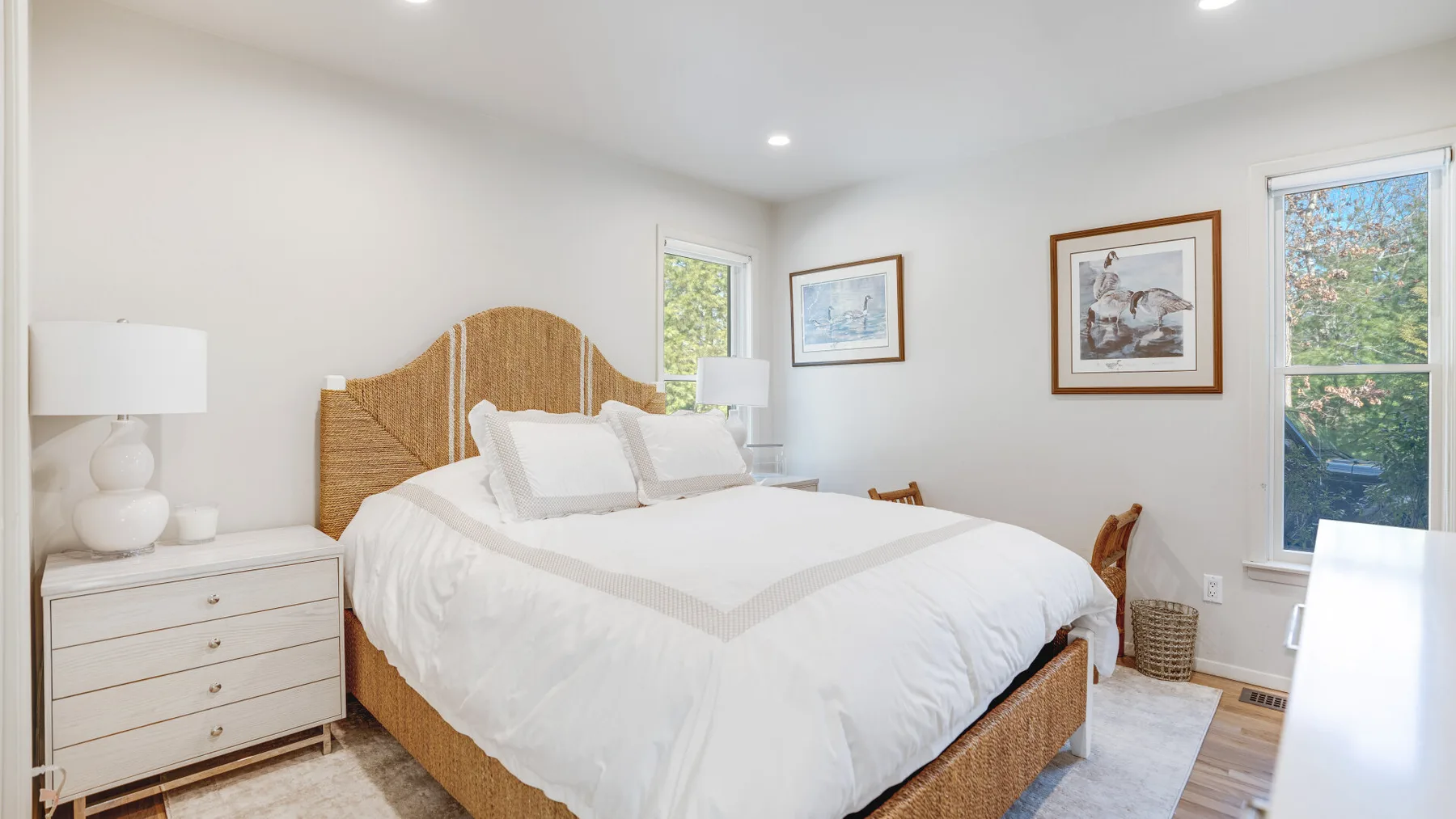 Un dormitorio luminoso con una cama grande, muebles auxiliares y ventanas.