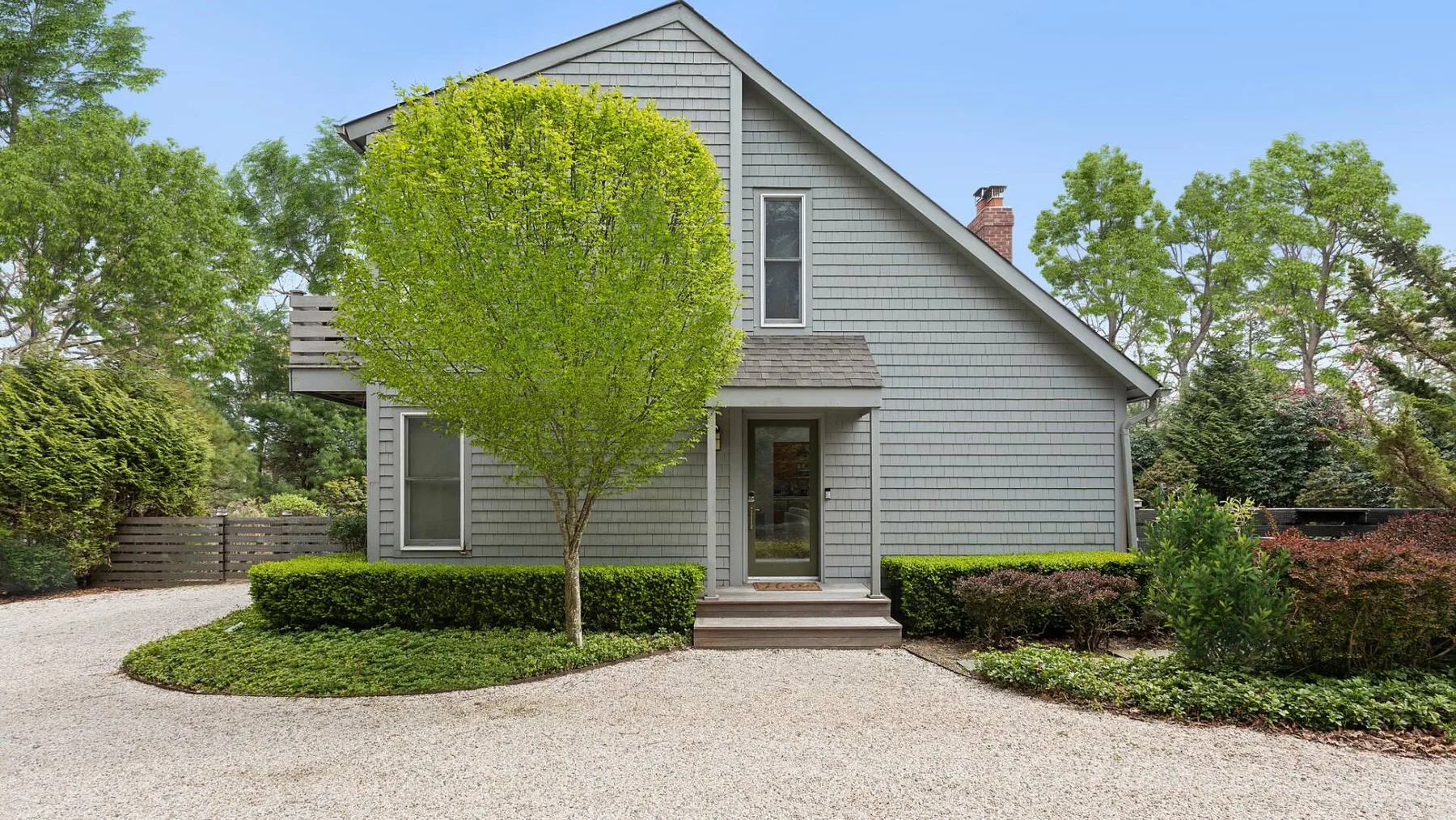 A gray-sided house stands behind a curved gravel driveway and landscaped shrubs.