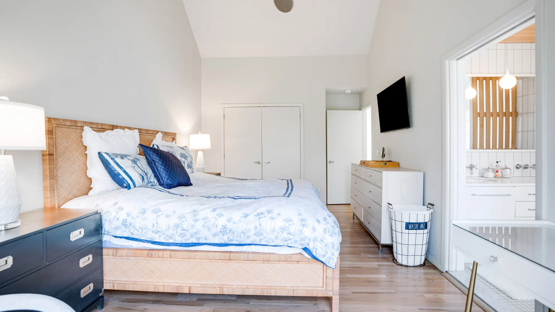 Un dormitorio luminoso con una cama, una cómoda y una puerta abierta al baño.