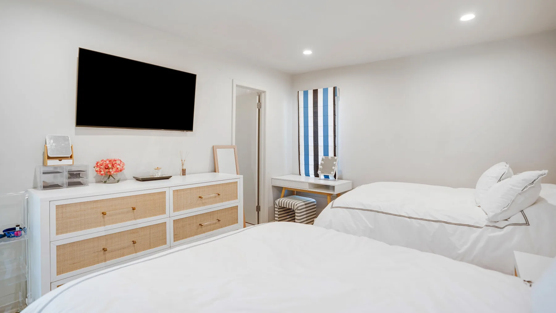 Un dormitorio luminoso con dos camas y una cómoda bajo un televisor montado en la pared.