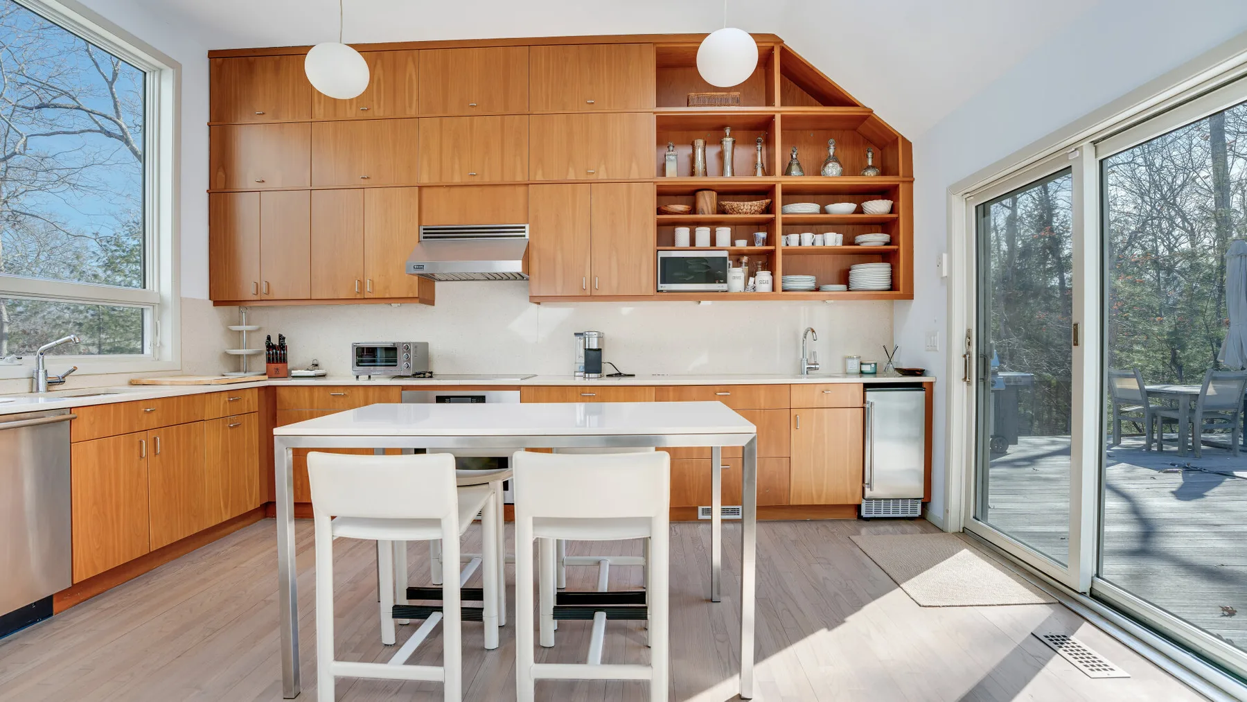 Una cocina y comedor luminosos con gabinetes de madera, una mesa y ventanas grandes.