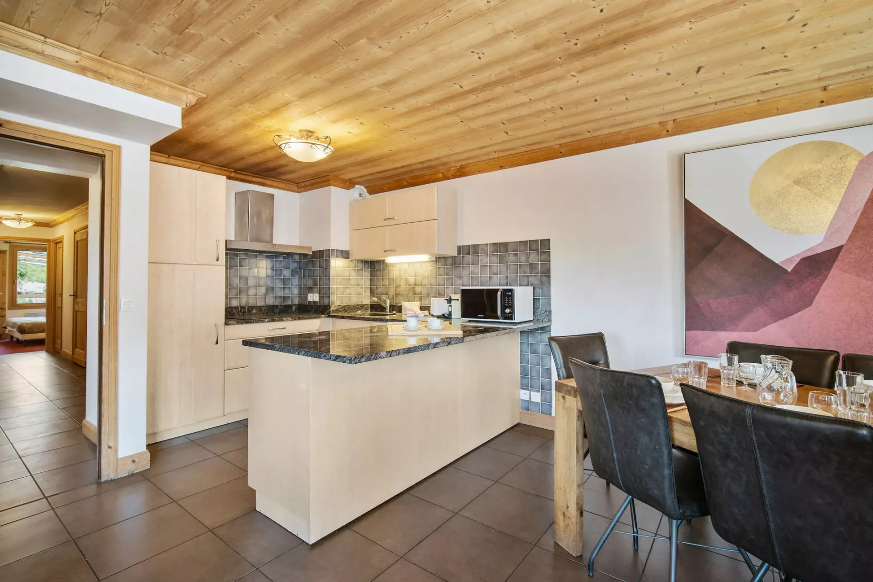 A kitchen with an island and an adjoining dining table beneath a wood-paneled ceiling.