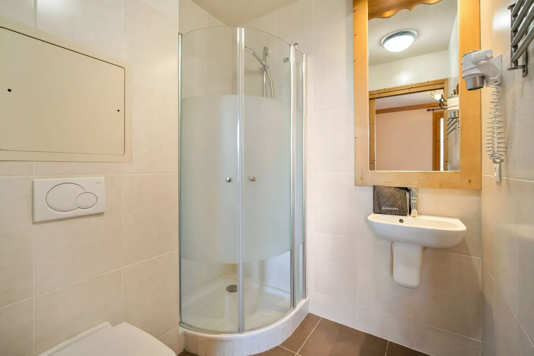 Un baño alicatado con una ducha de vidrio curvada y un lavabo de pared.