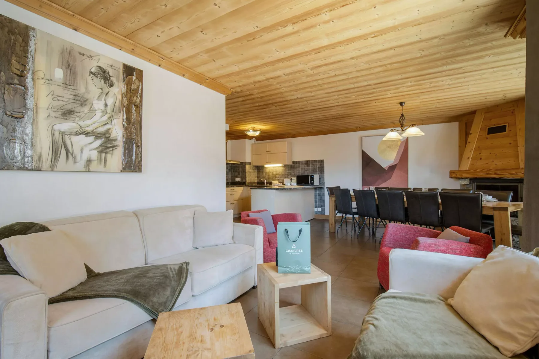 Una sala y comedor con asientos claros, techo de madera y cocina abierta.