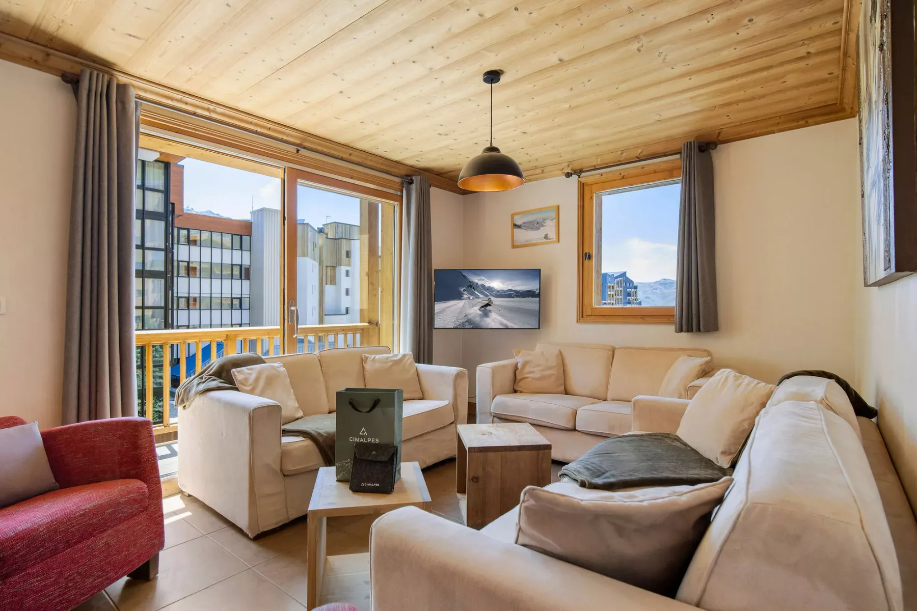 Una sala de estar luminosa con asientos beige, grandes ventanas y techo de madera.