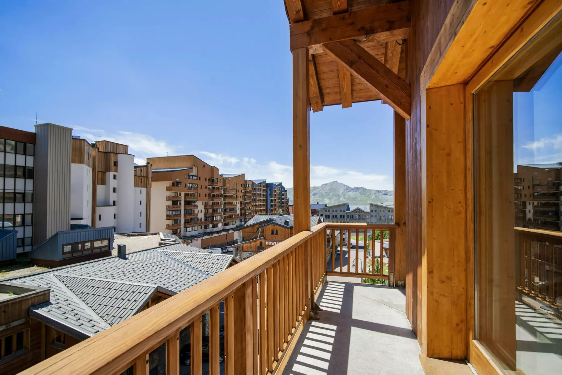 A wooden balcony overlooks nearby buildings and distant mountains.