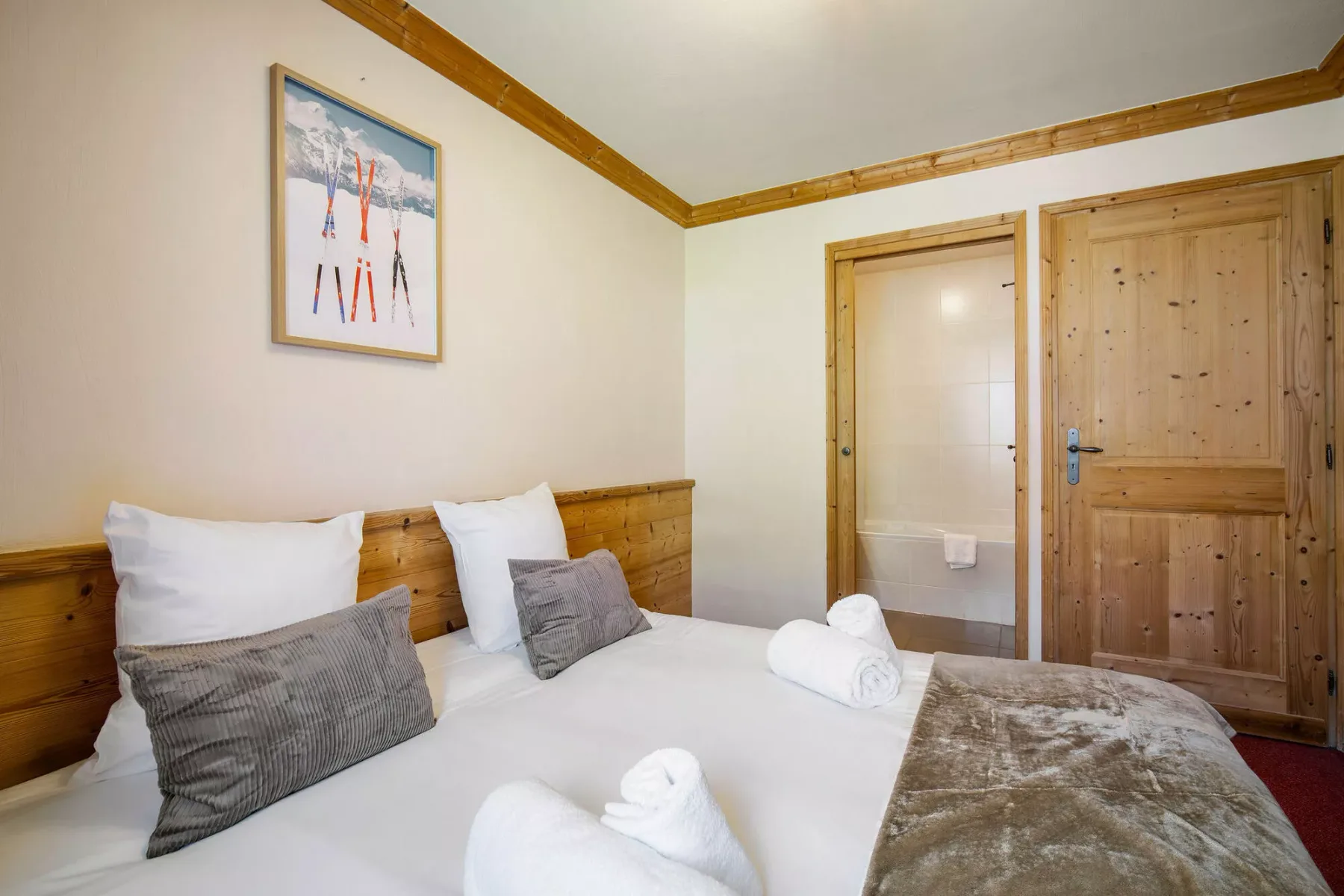 Un dormitorio con una cama, una obra enmarcada y una puerta de madera junto al baño.