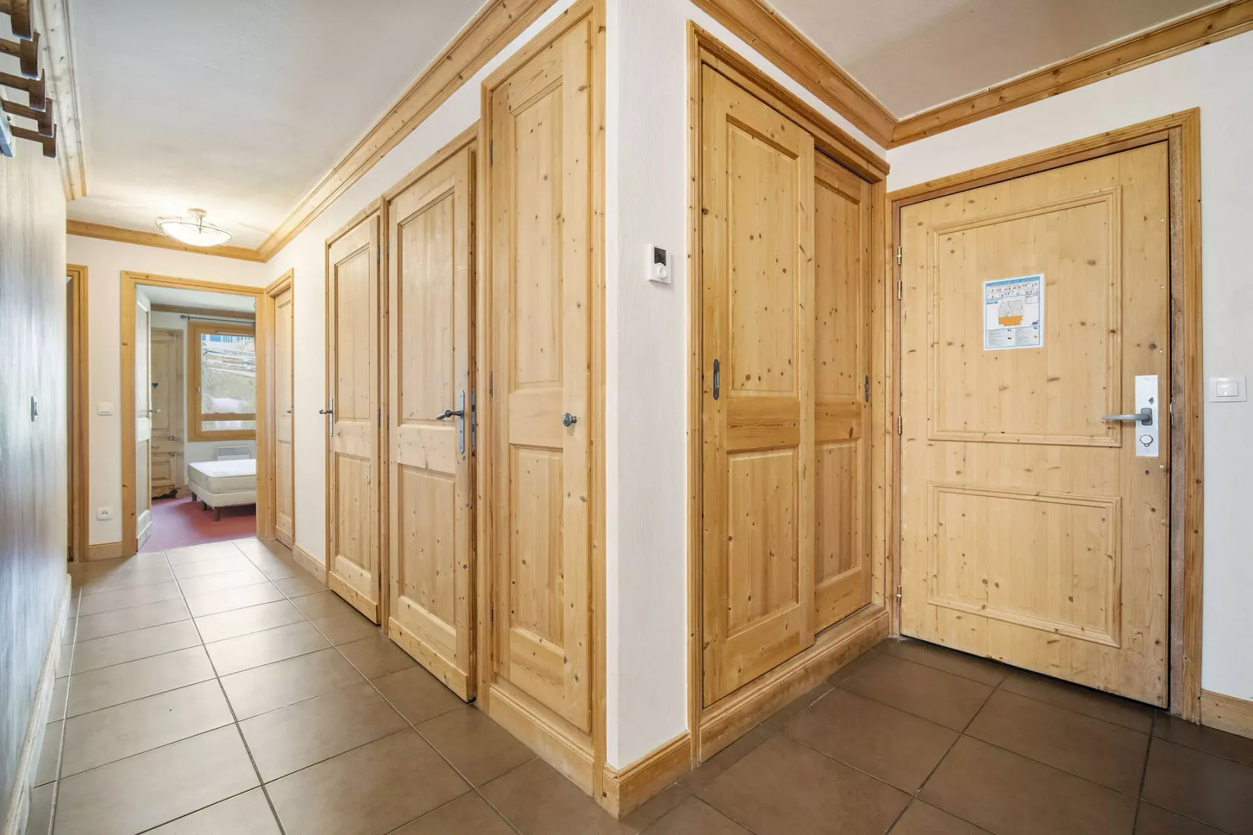 Un pasillo revestido de madera con varias puertas y suelo de baldosas.