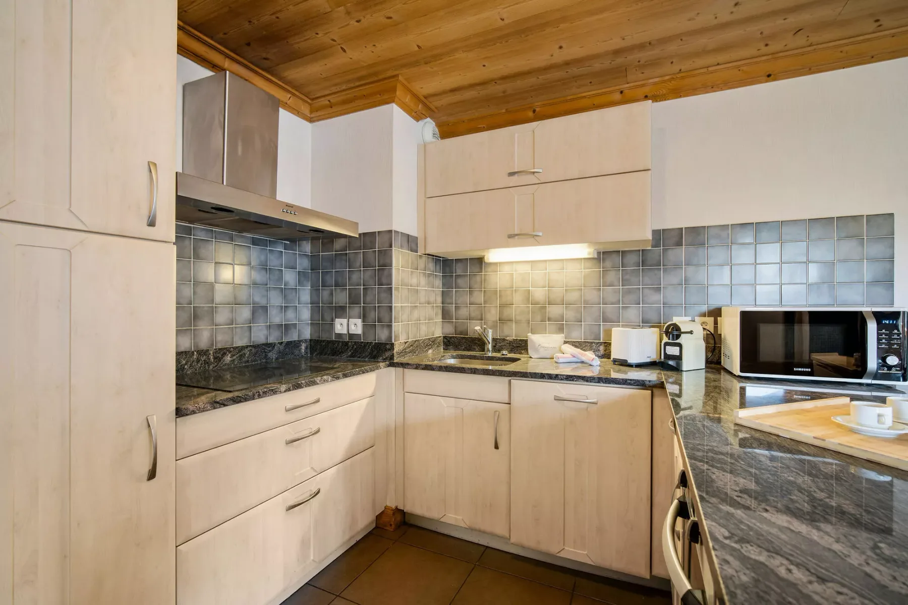 Una cocina con gabinetes de madera clara, encimeras oscuras y salpicadero de azulejos.