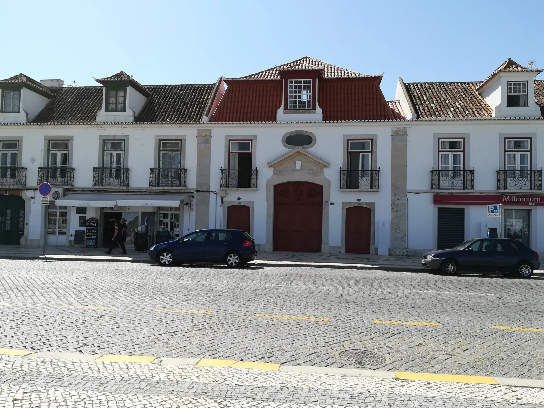 Una fila de edificios blancos da a una calle adoquinada, con coches aparcados junto a la acera.