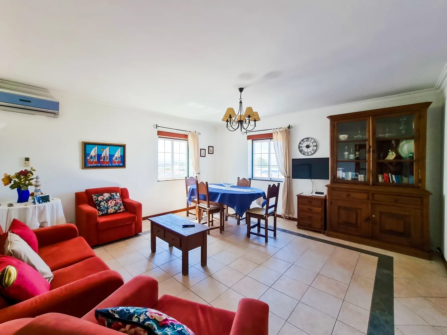 Sala de estar y comedor con asientos rojos, una mesa y una vitrina de madera.