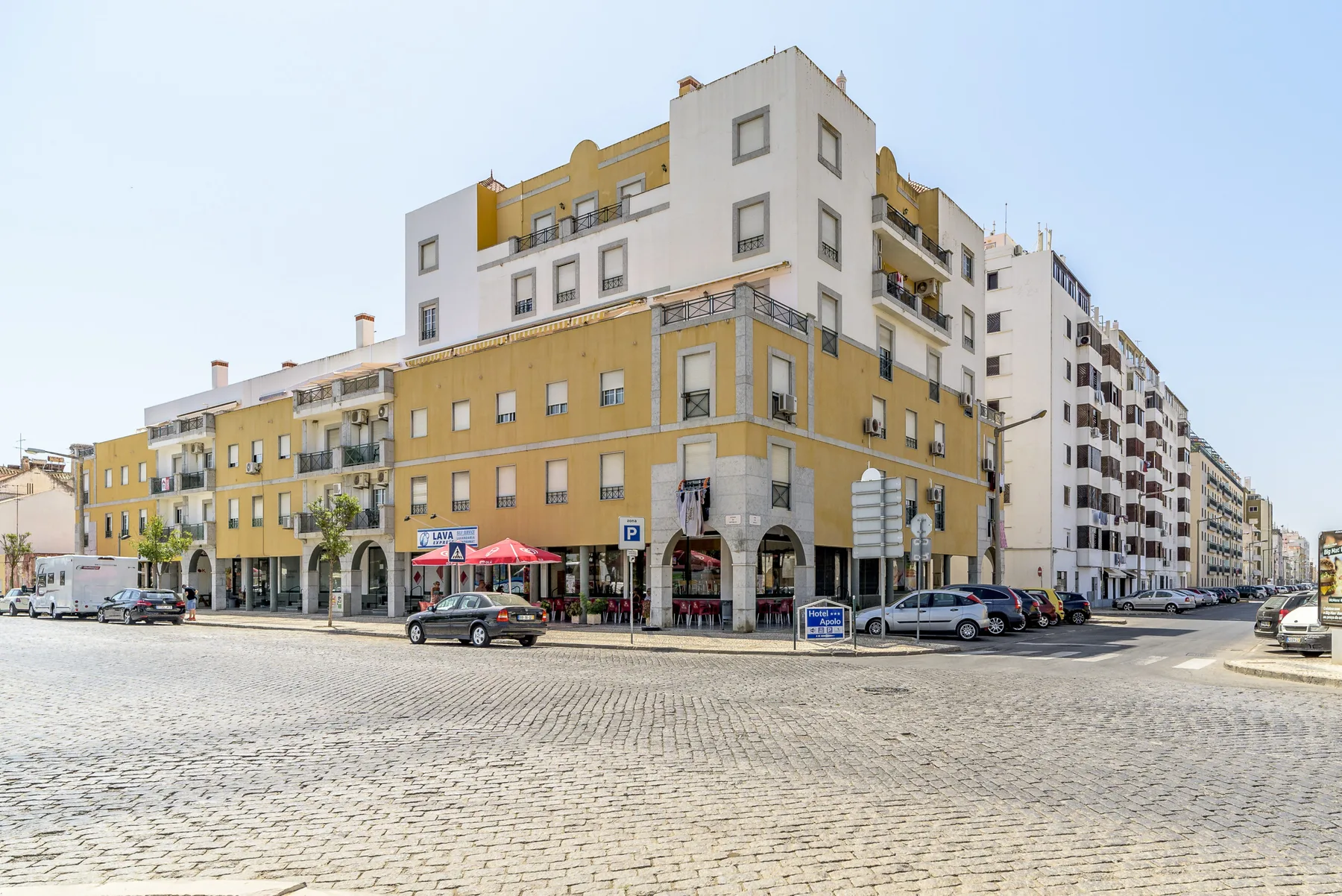 Una esquina urbana con edificios de varias plantas y coches junto a una calle empedrada.