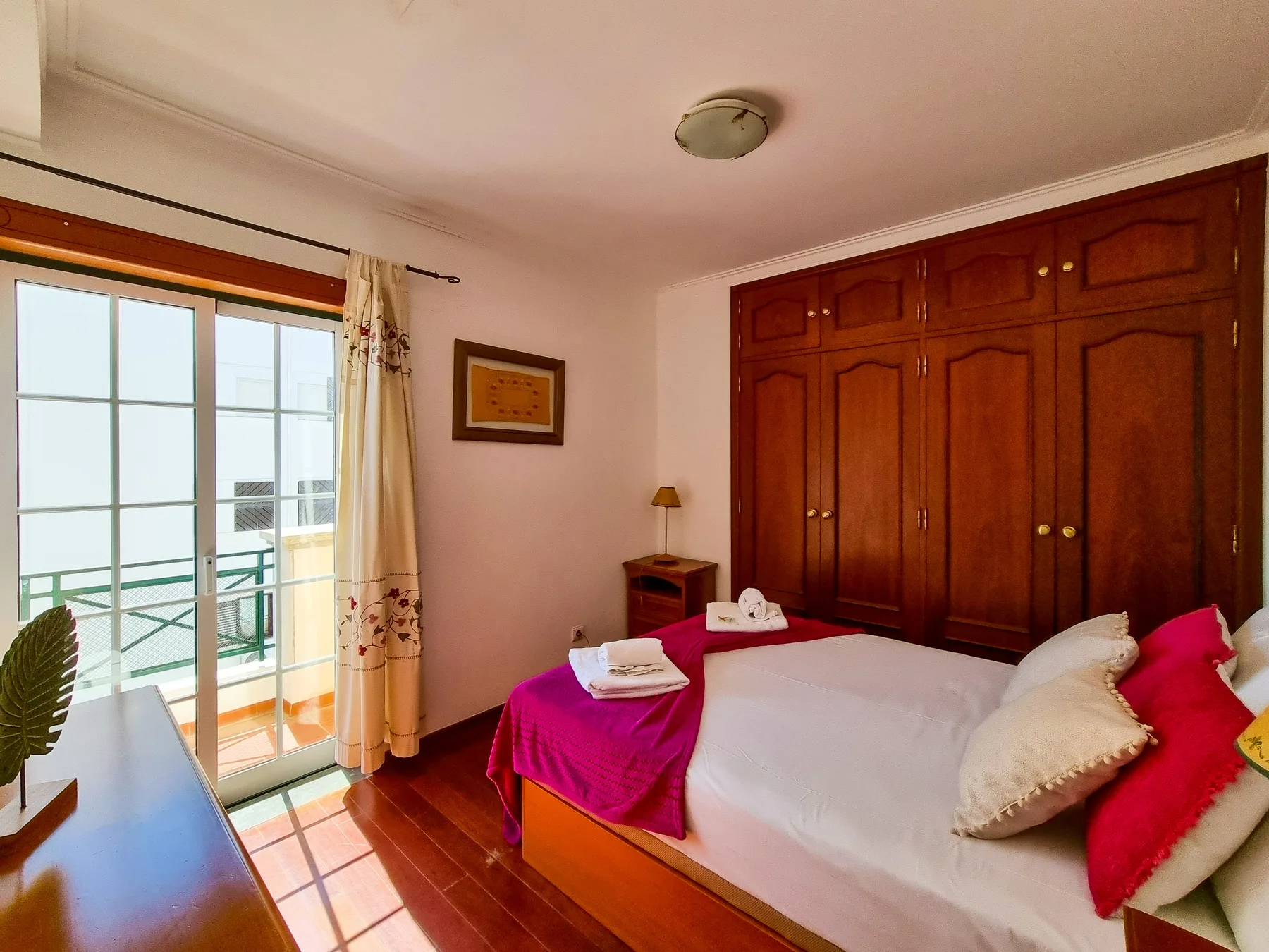 Un dormitorio con una cama junto a un armario grande de madera y una ventana luminosa.