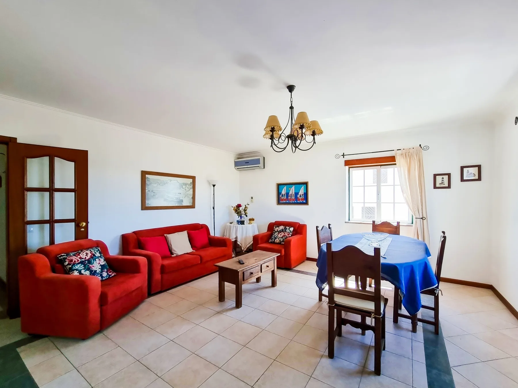 Una luminosa sala de estar y comedor con asientos rojos y una mesa cubierta de azul.