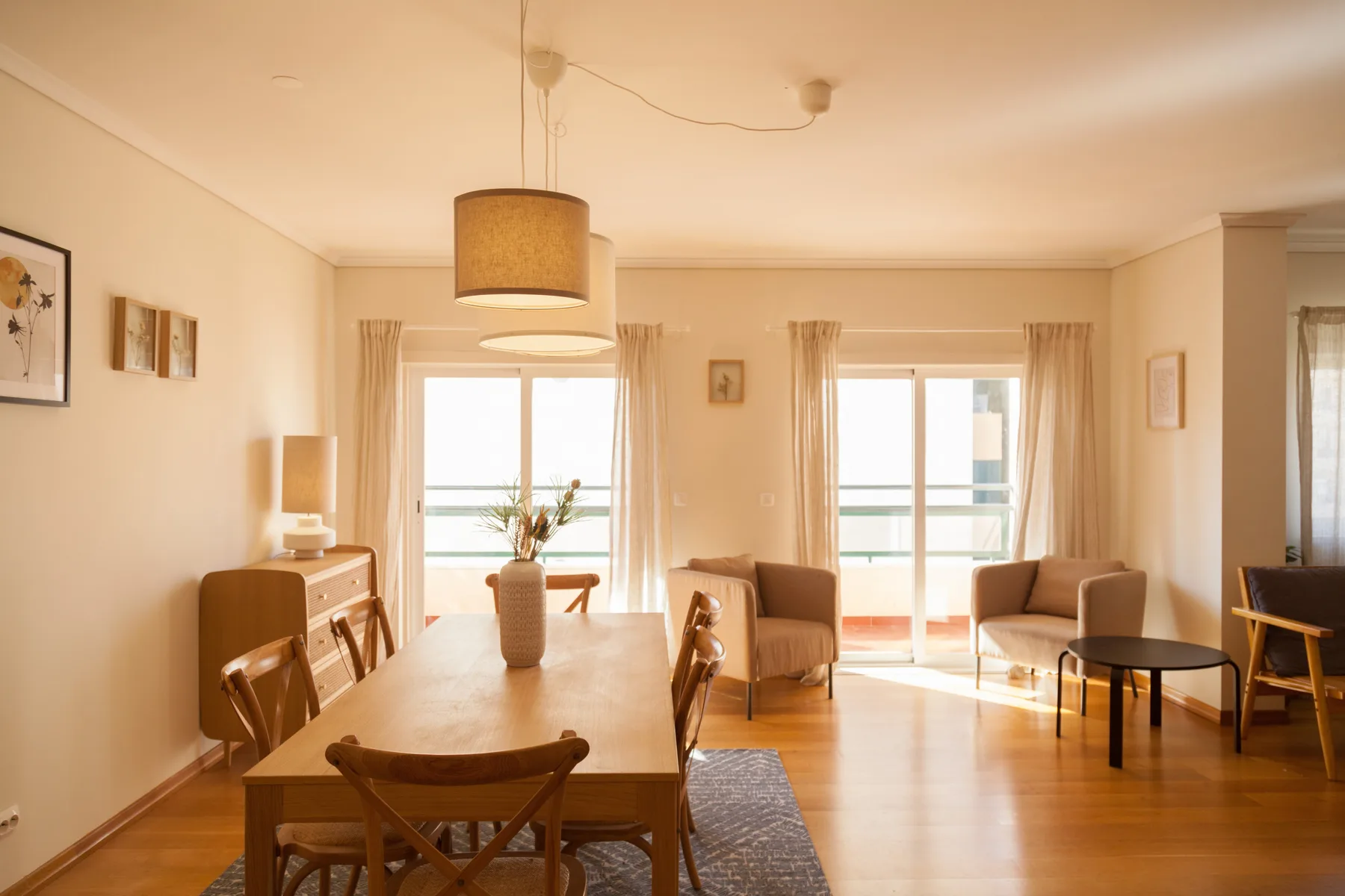 Un luminoso salón-comedor con una mesa de madera y asientos junto a grandes ventanales.