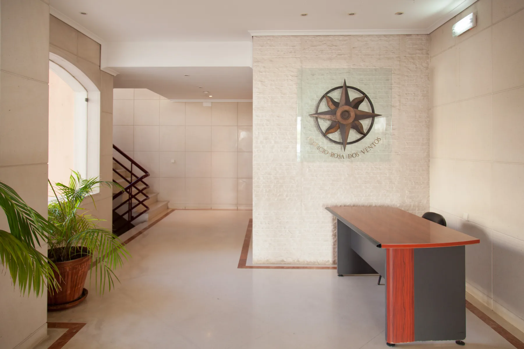 Un vestíbulo luminoso con mostrador de recepción, paredes de azulejos y plantas en macetas.