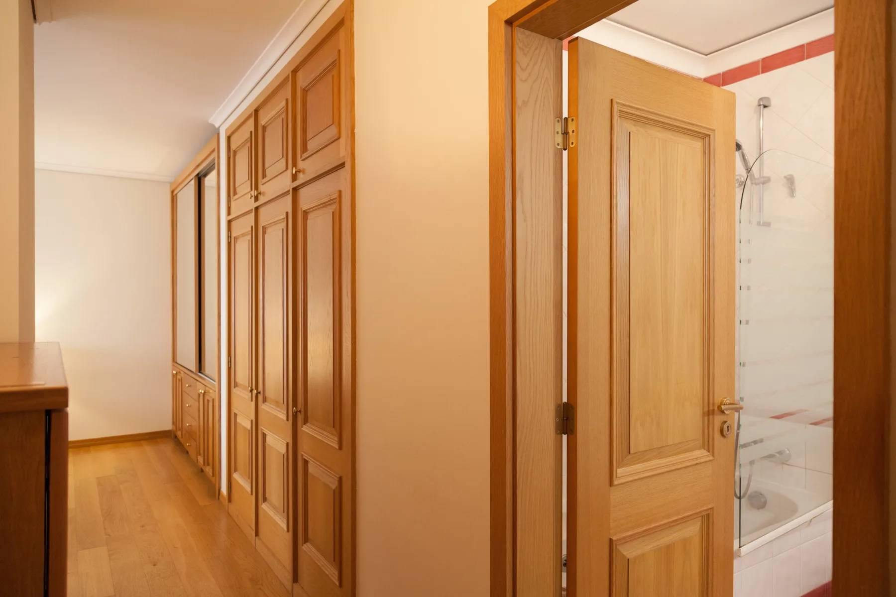 Un pasillo con puertas de madera conduce a un baño con ducha.