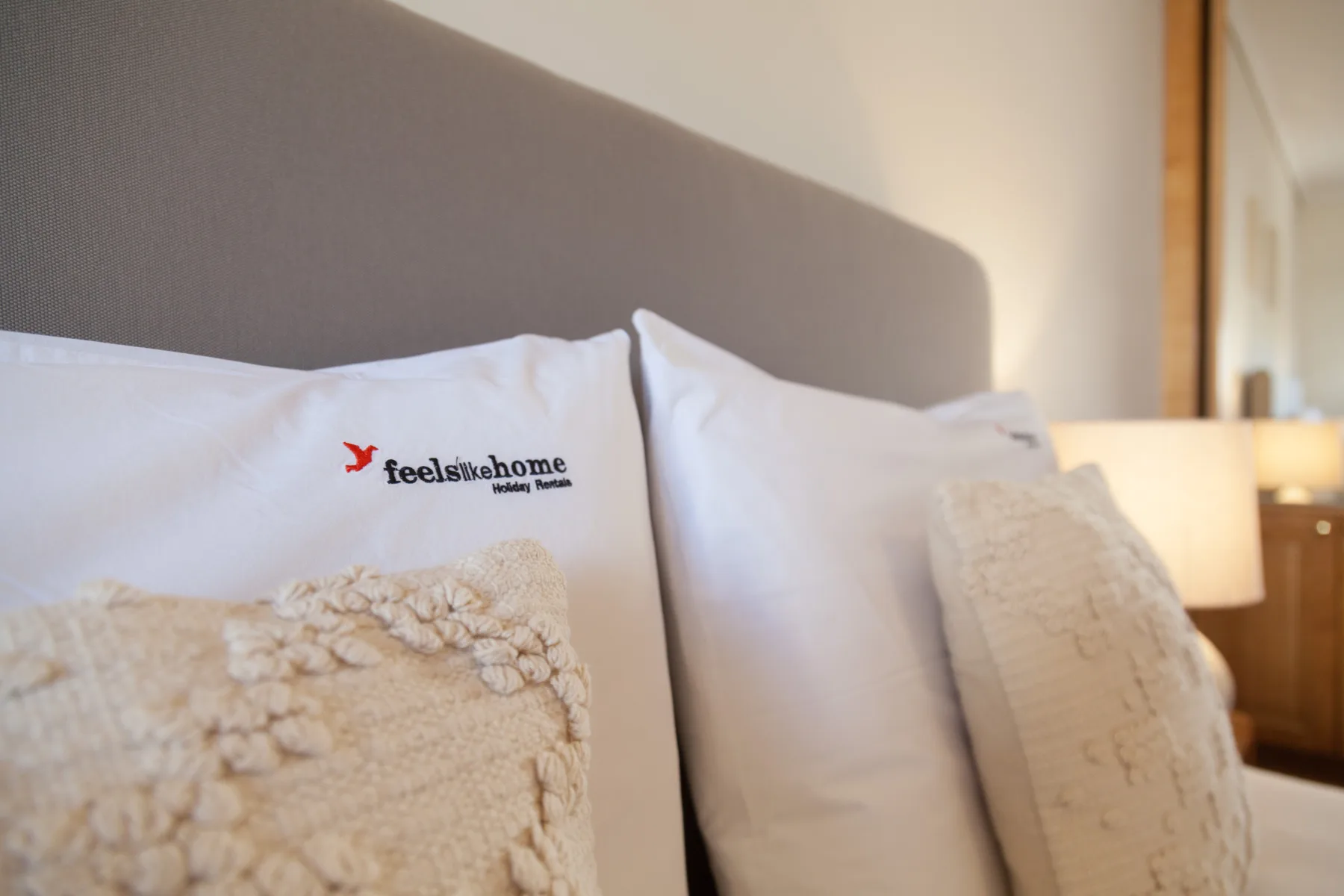 Dormitorio con almohadas blancas y cojines texturizados junto a un cabecero acolchado.