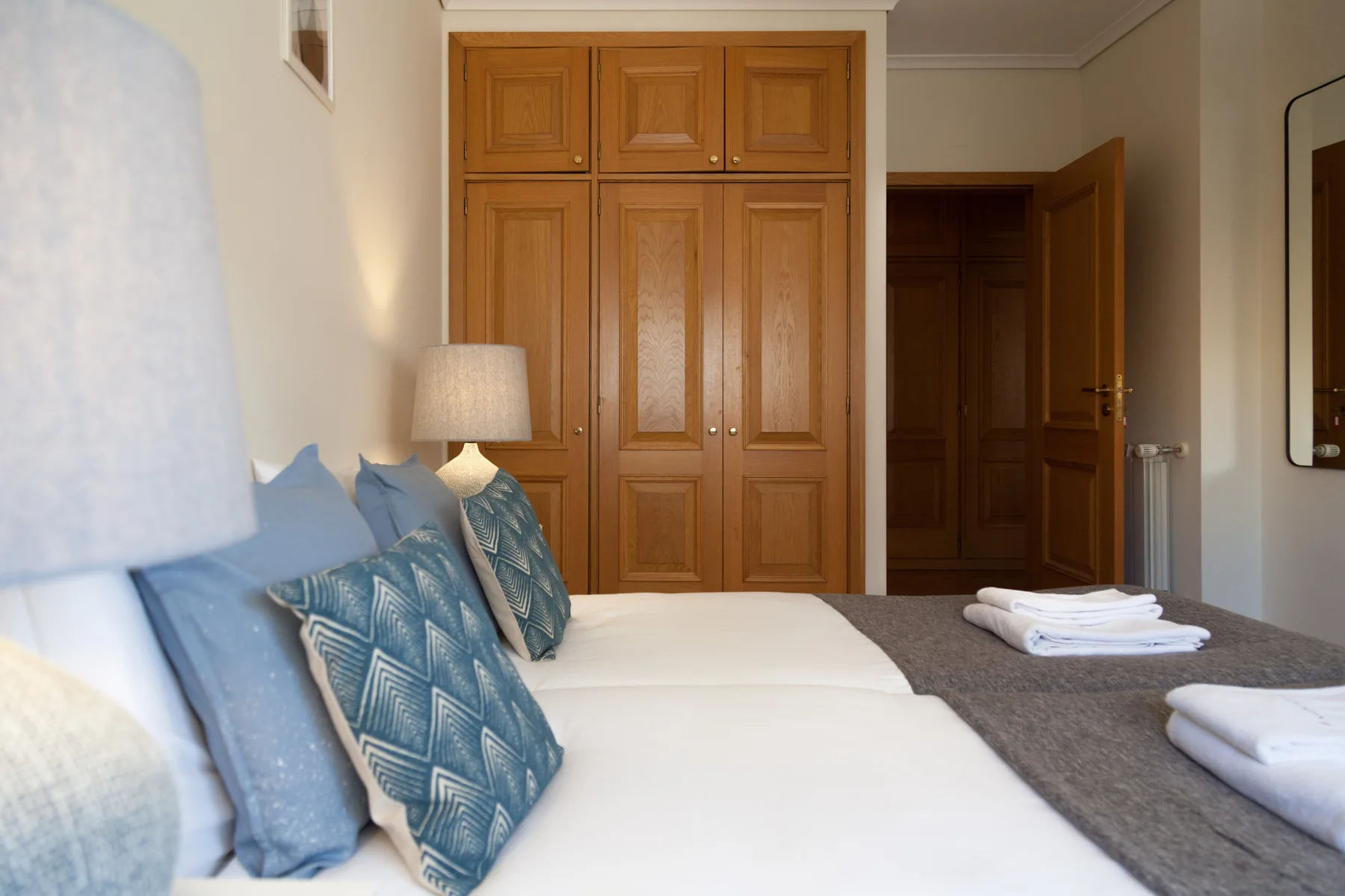 Dormitorio con dos camas, cojines azules estampados y armarios de madera.