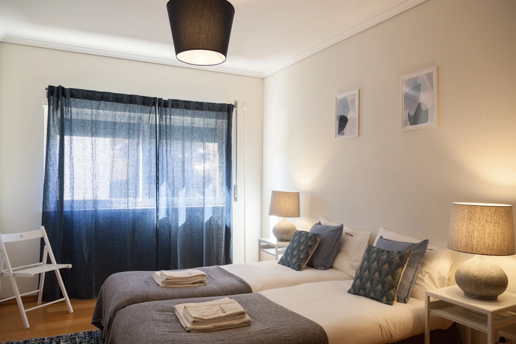 Un dormitorio con dos camas, cortinas oscuras y lámparas de mesilla.