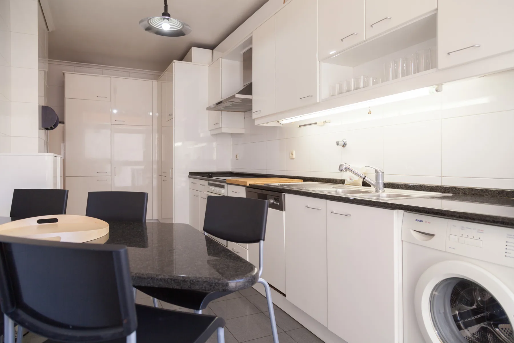 Una cocina luminosa con armarios blancos, una encimera y una mesa de comedor.