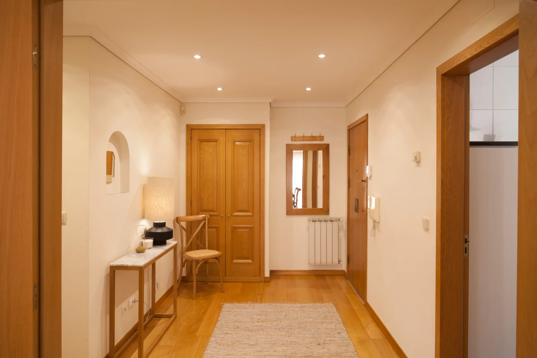 Un pasillo luminoso con puertas de madera, una consola y una alfombra alargada.