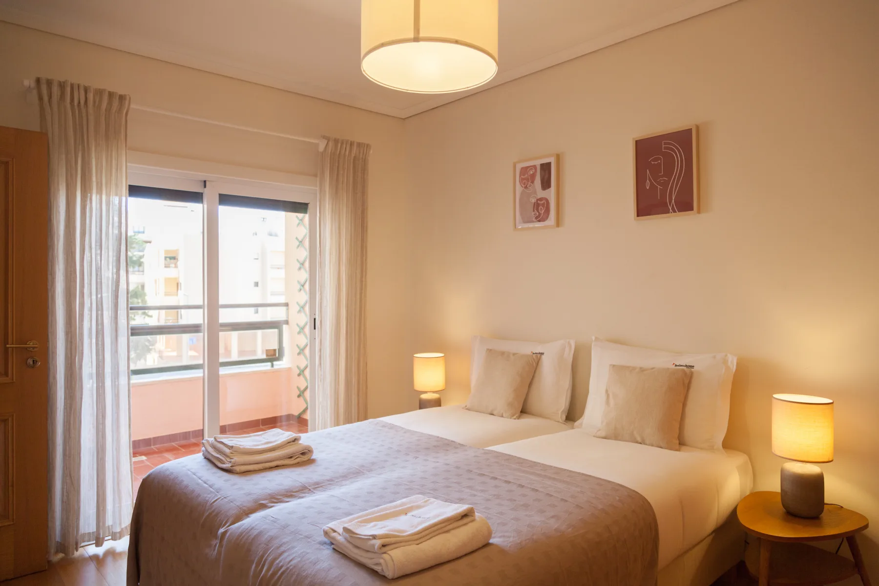 Un dormitorio con una cama doble, lámparas de noche y cortinas junto a una puerta de cristal.
