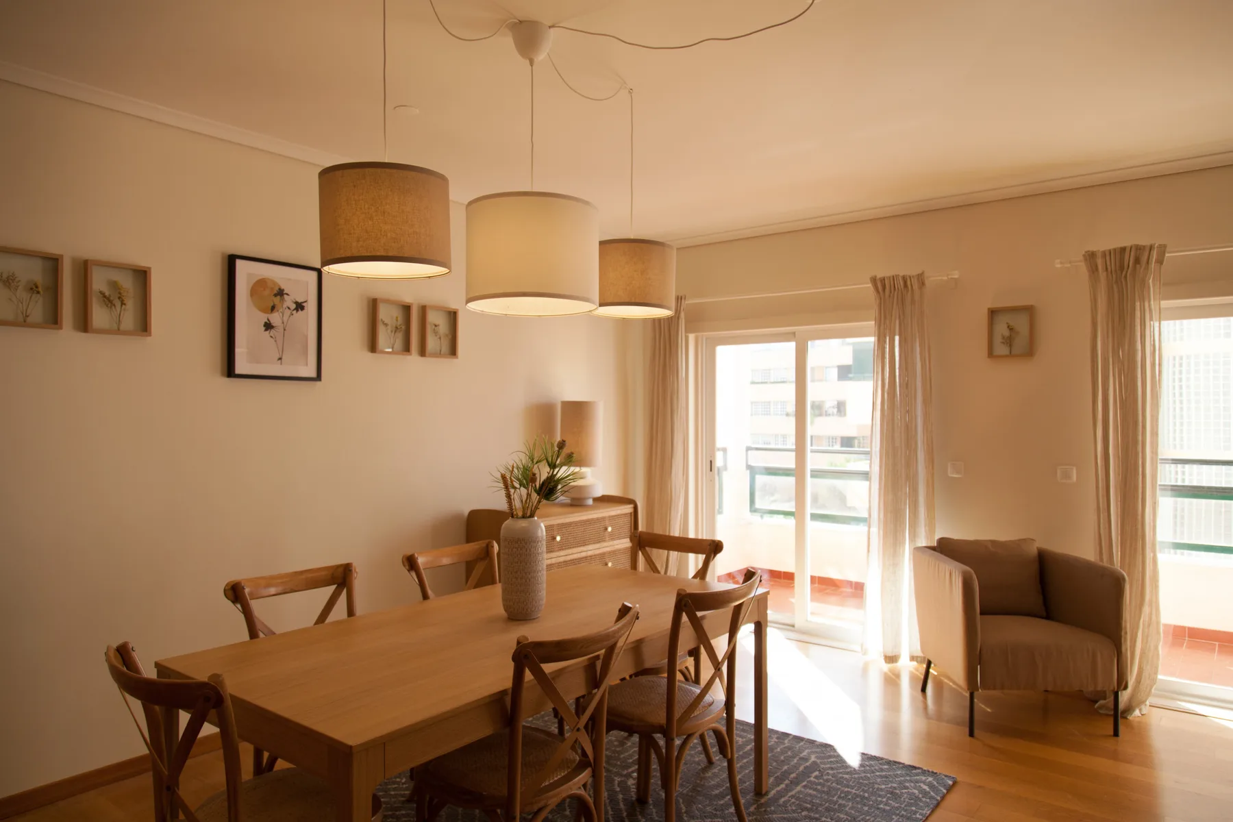 Zona de comedor y estar con una mesa de madera, asientos y ventanas luminosas.