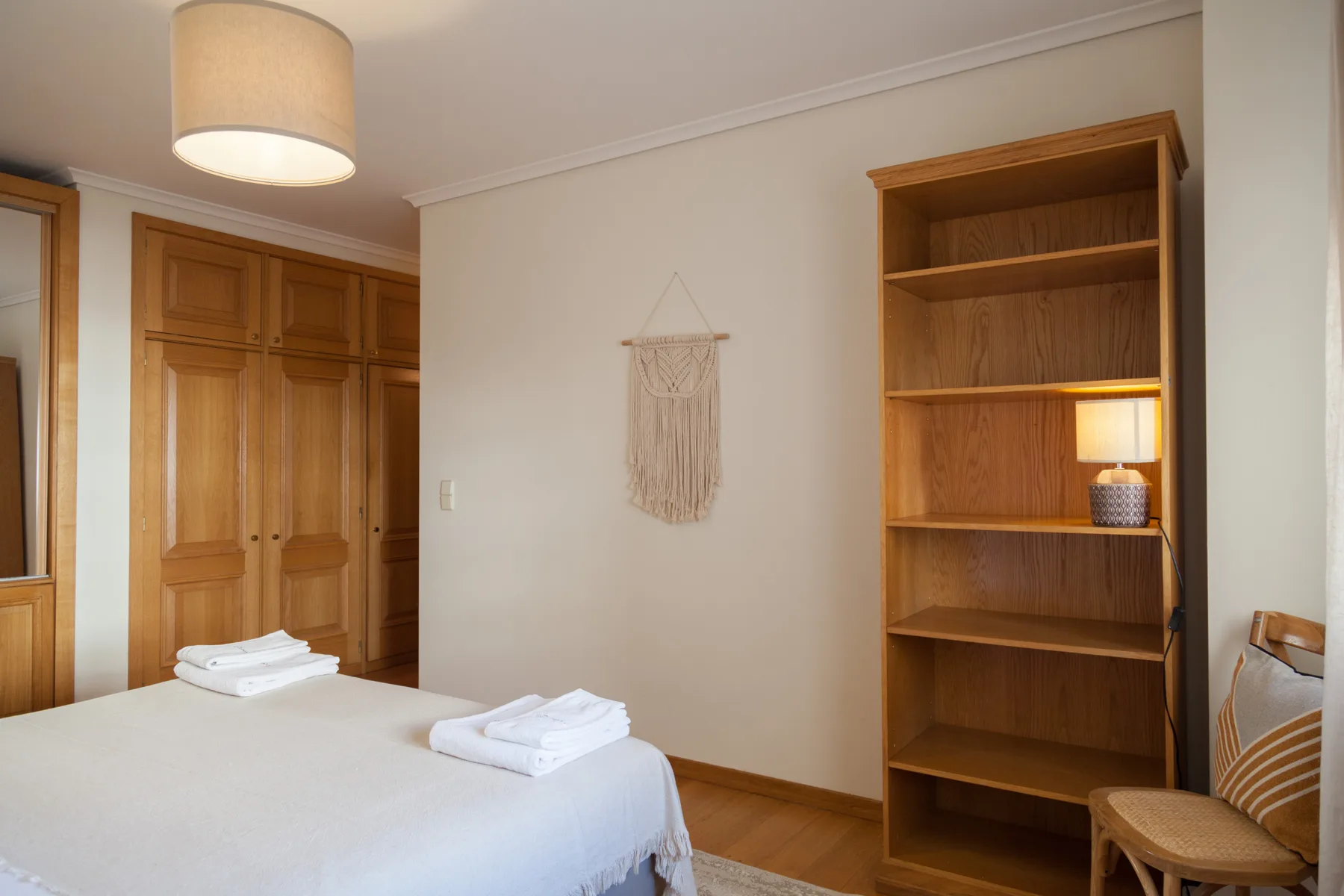 Dormitorio con una cama bien arreglada, armario de madera y estanterías abiertas.
