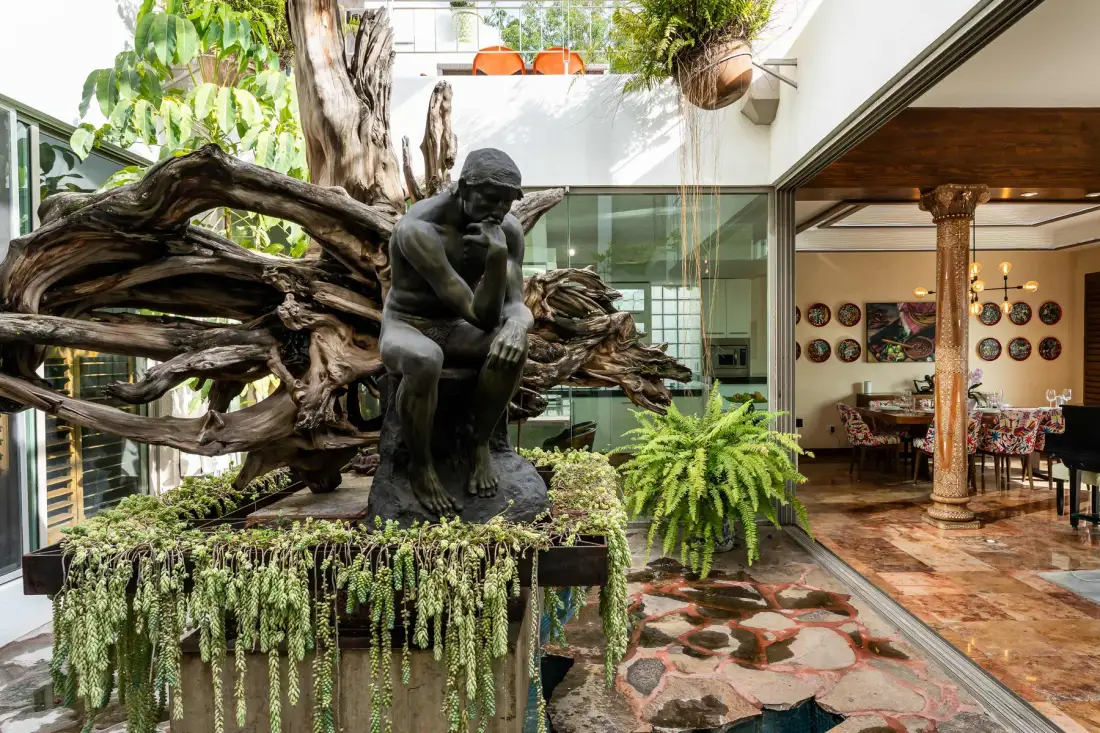 An indoor courtyard features a seated sculpture, greenery, and an adjoining dining area.