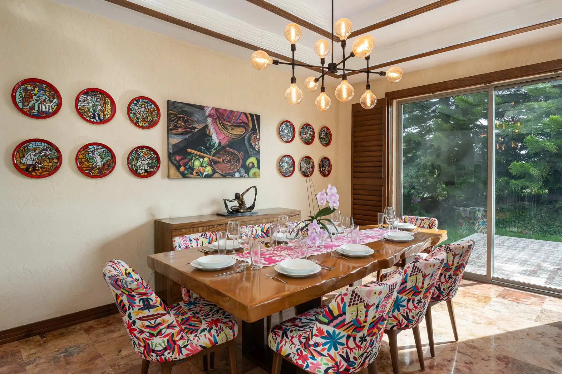 A dining area with a wooden table, colorful seating, and a large glass door.