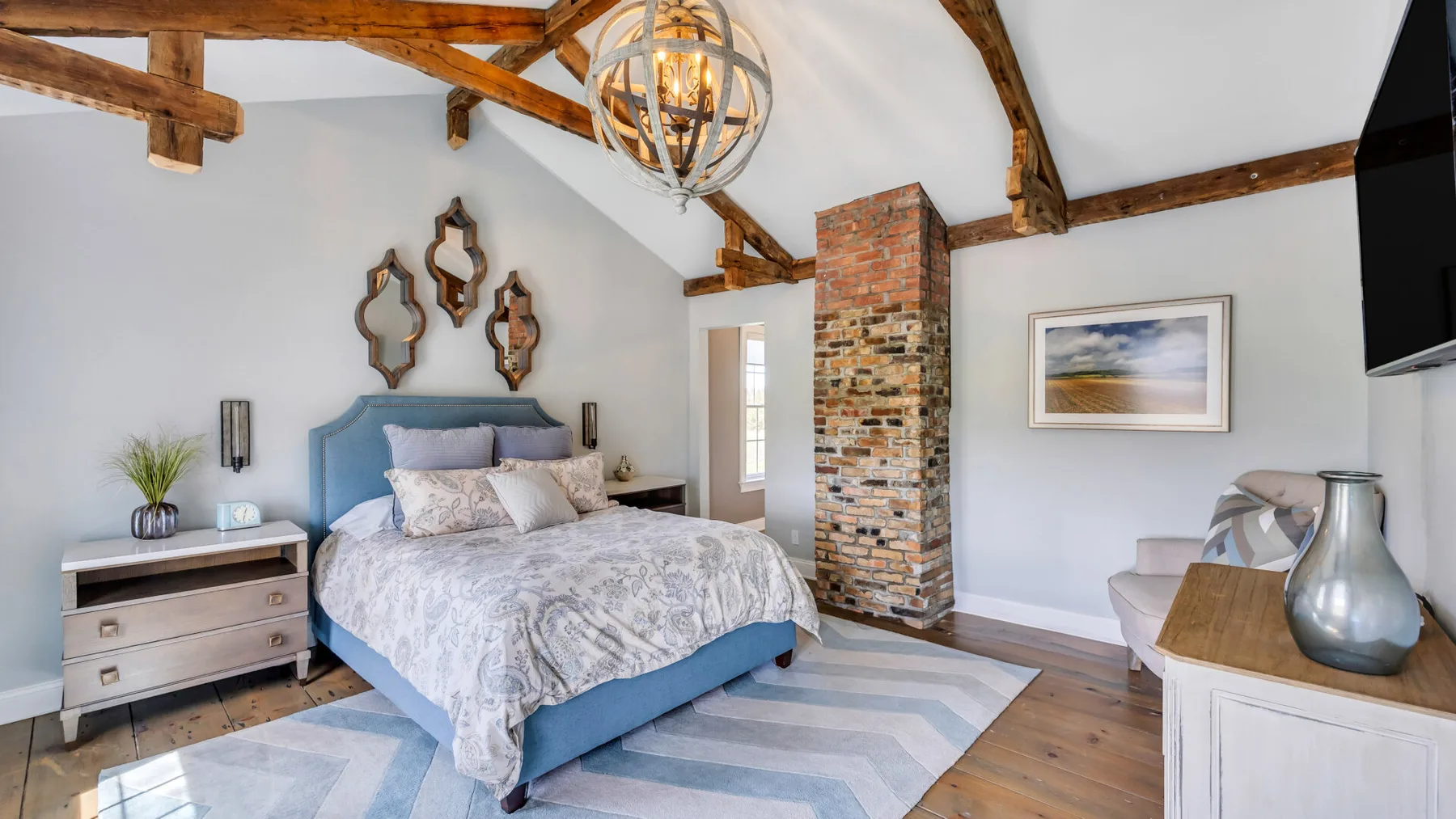 Un dormitorio con una cama, vigas de madera a la vista y una columna de ladrillo.