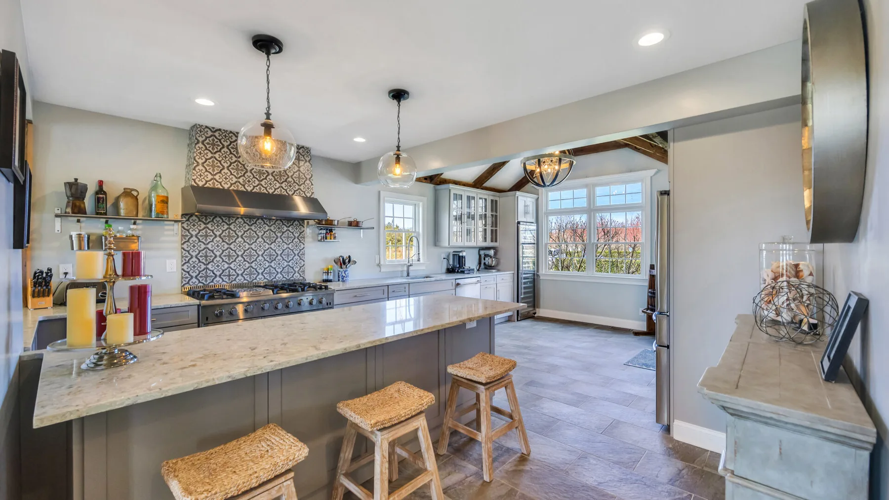 Una cocina luminosa con una isla larga, taburetes y luces colgantes.